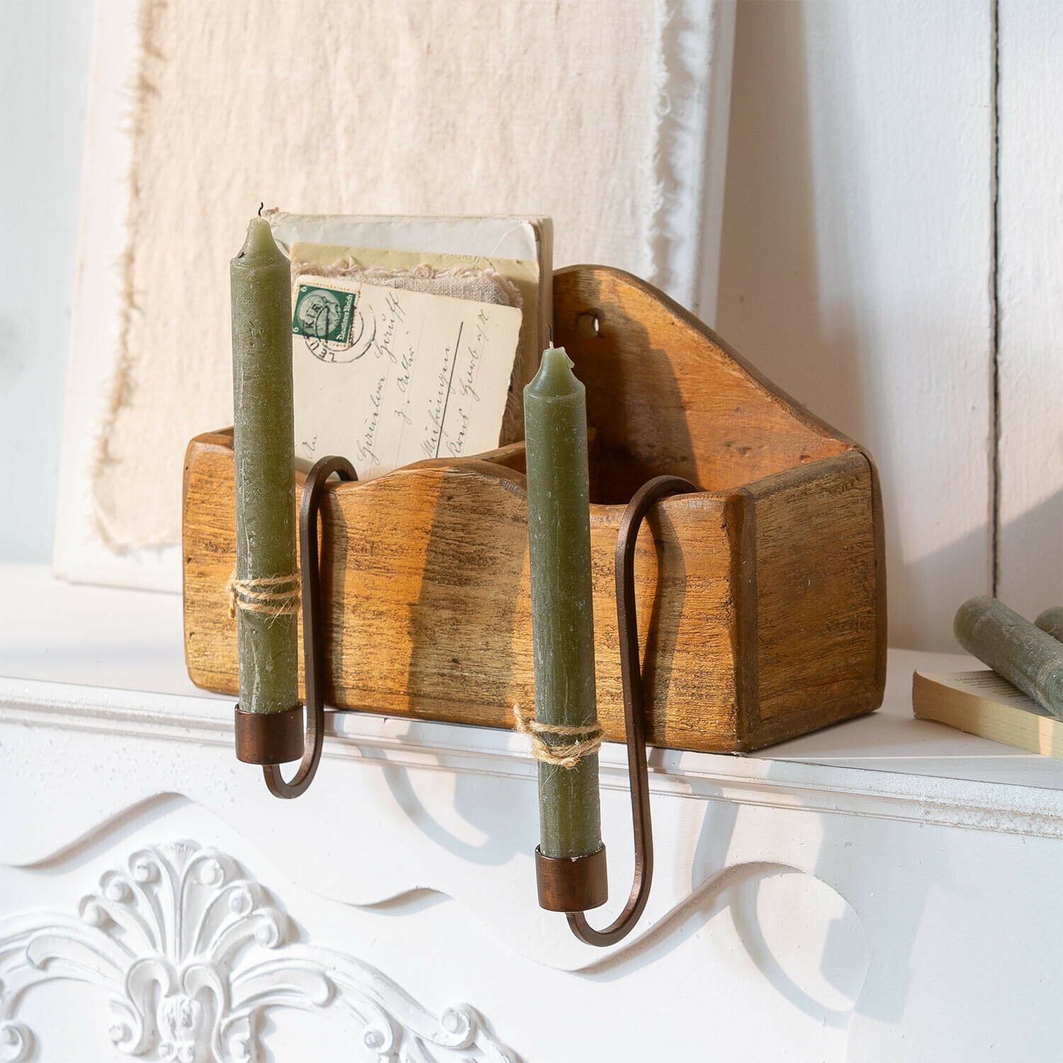 Organizer in legno con candele verdi e supporti metallici su camino bianco
