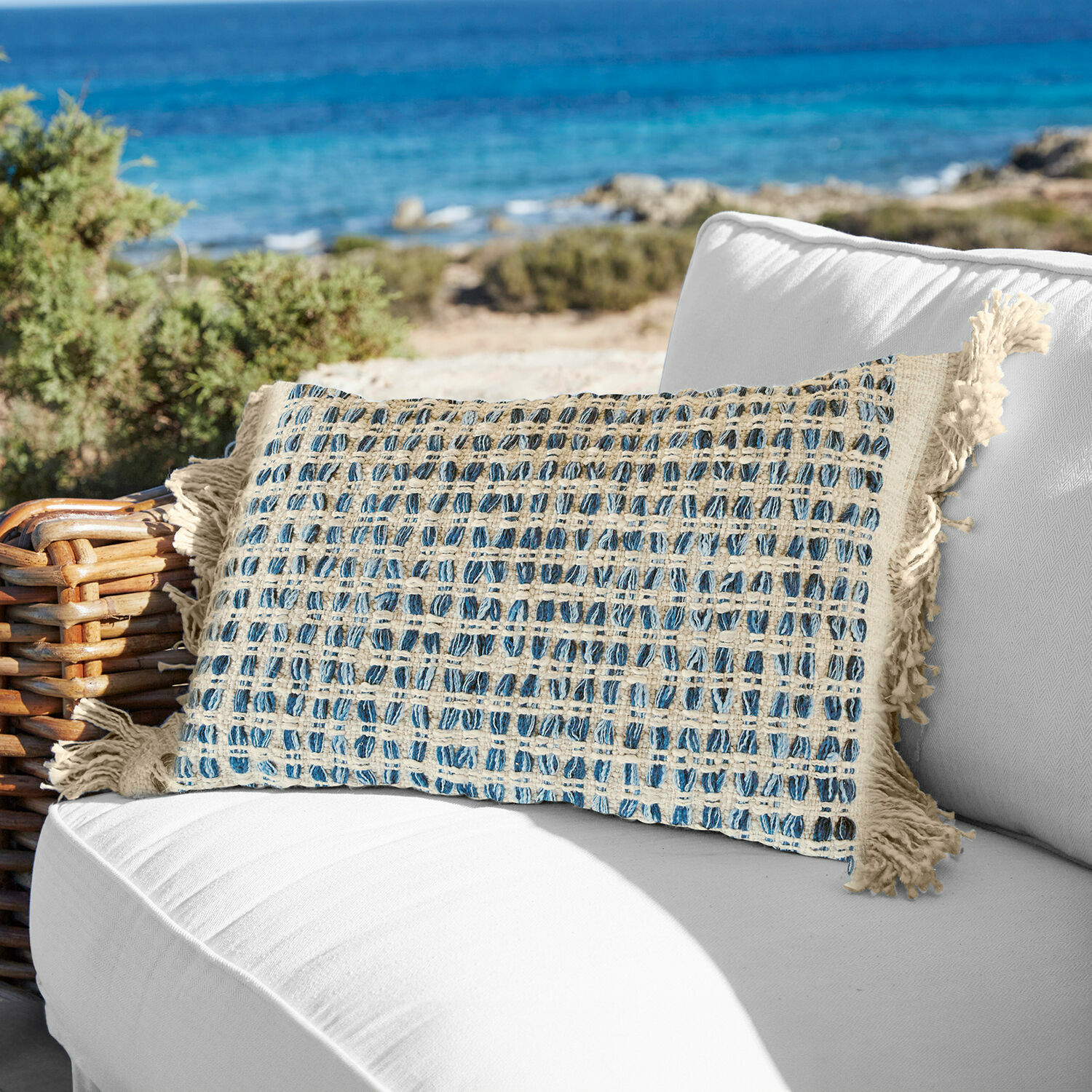 Copricuscino Monrovie Cuscino decorativo in cotone crema e blu a quadri con frange su divano bianco all'aperto