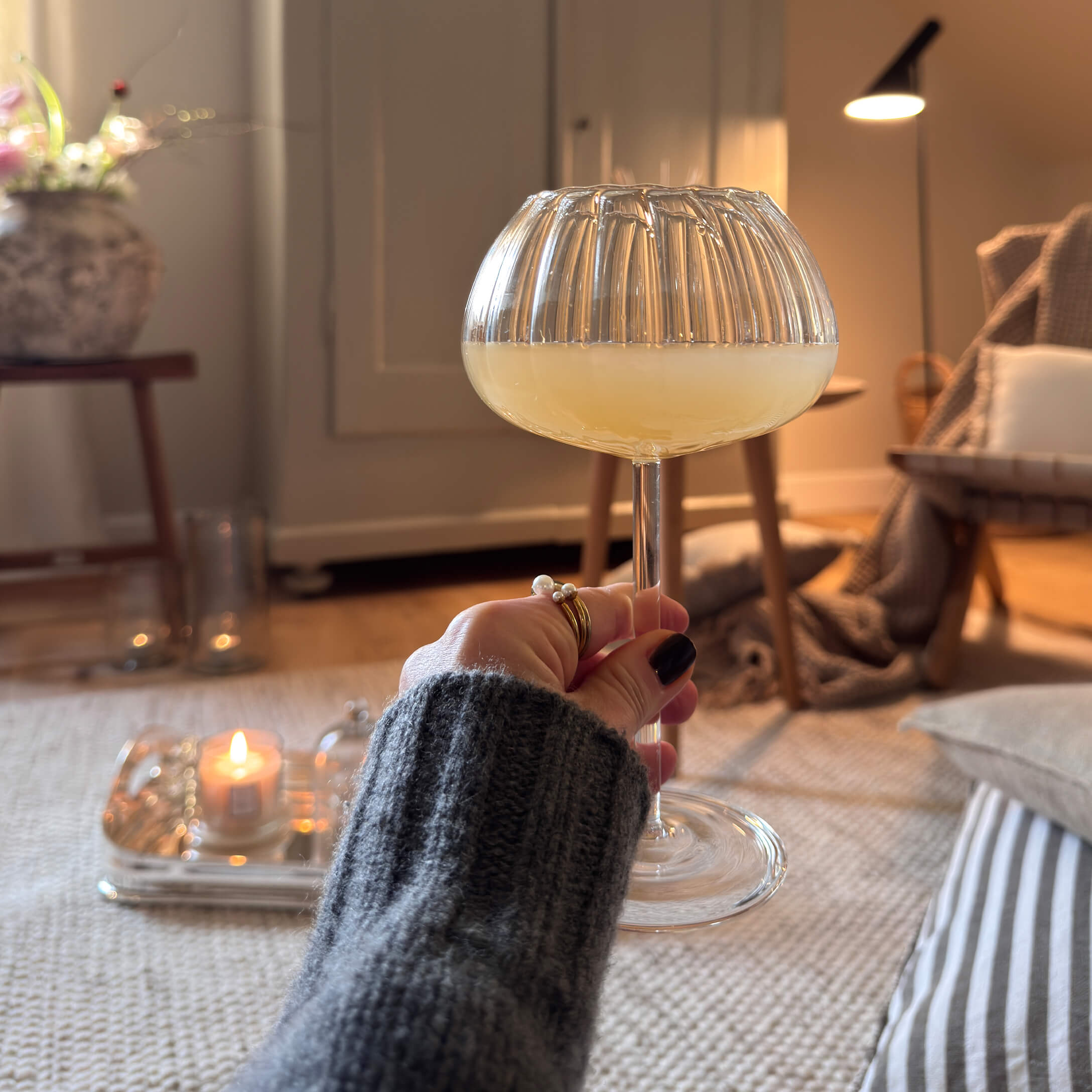 Mano che tiene un bicchiere con bevanda gialla in un interno accogliente con luce soffusa e decorazioni
