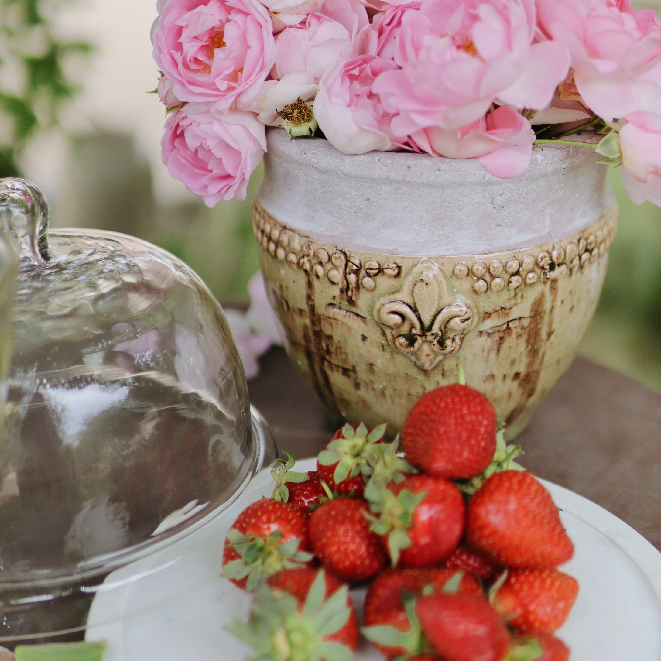 Vaso in ceramica con fiori rosa e fragole fresche su un piatto bianco