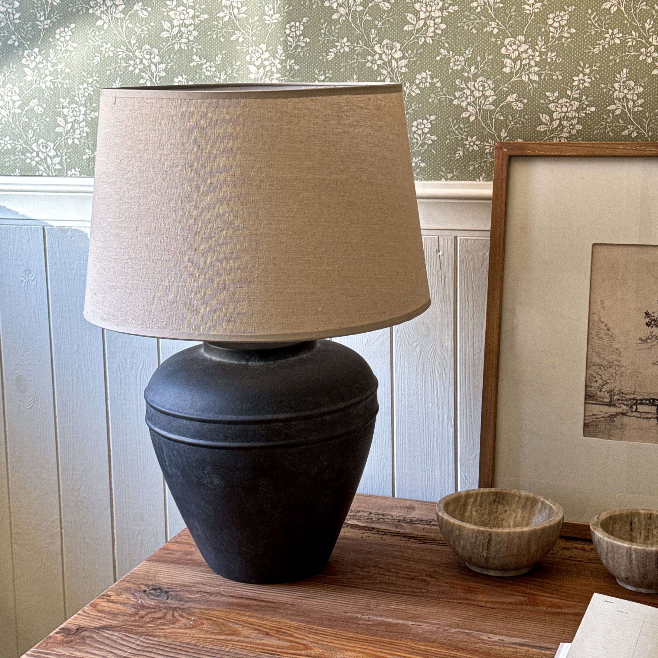 Lampada da tavolo con base in ceramica nera e paralume beige su tavolo in legno