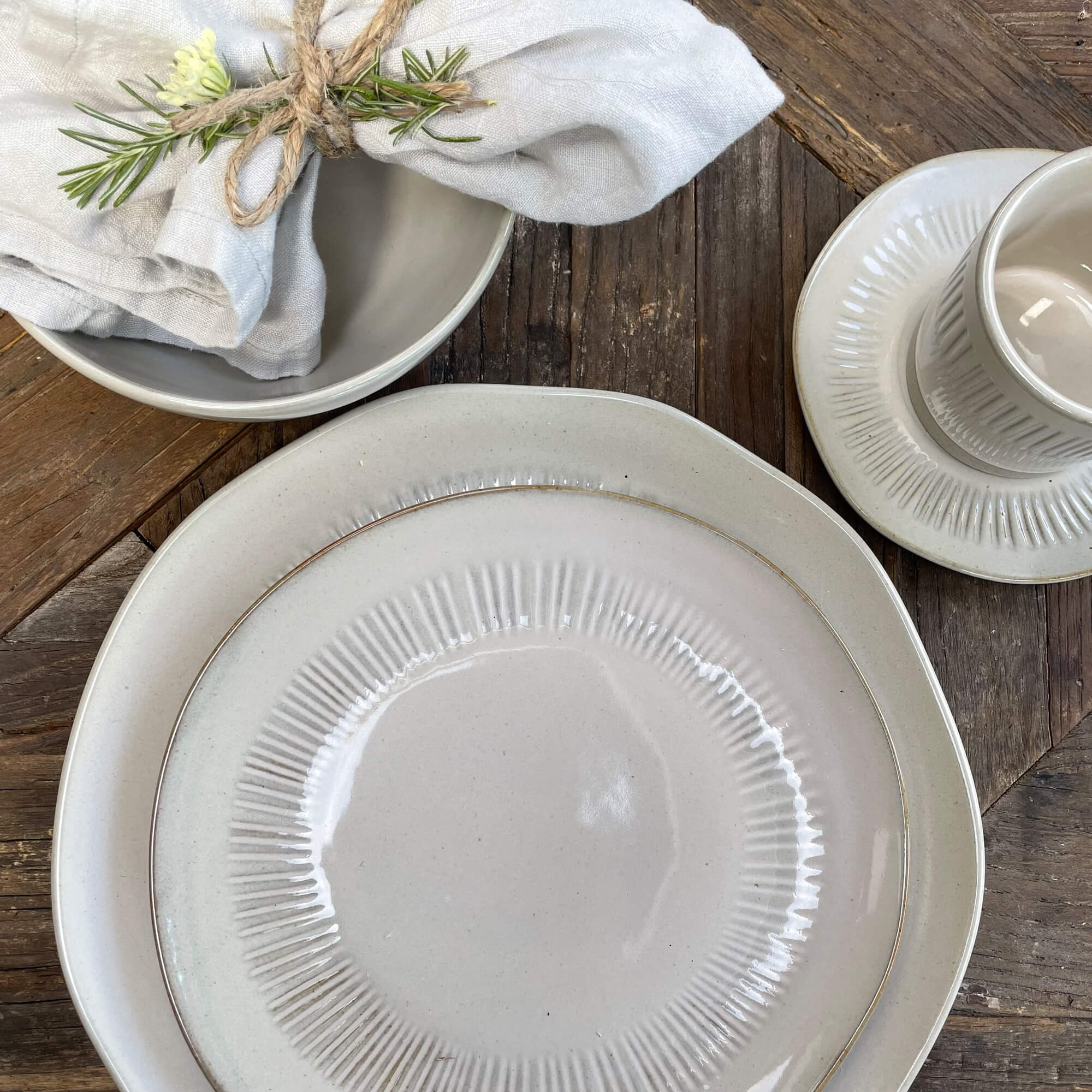 Set di stoviglie in ceramica crema con piatti e tazza su tavolo in legno, decorazione di lino e rosmarino