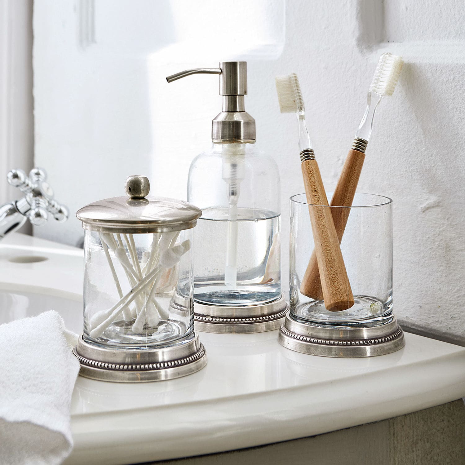 Set per bagno Drinapoly Accessori da bagno in vetro con dettagli metallici su lavabo bianco con spazzolini da denti in bambù