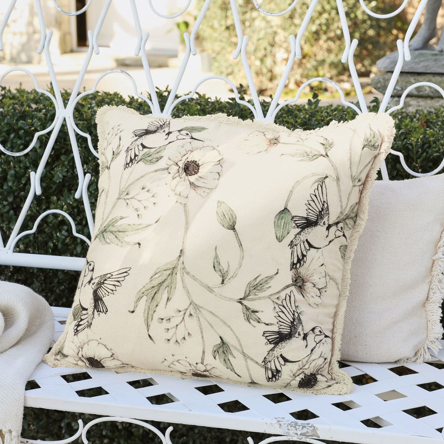 Copricuscino Byrne Cuscino decorativo beige con motivo di uccelli e fiori su panchina metallica bianca in giardino