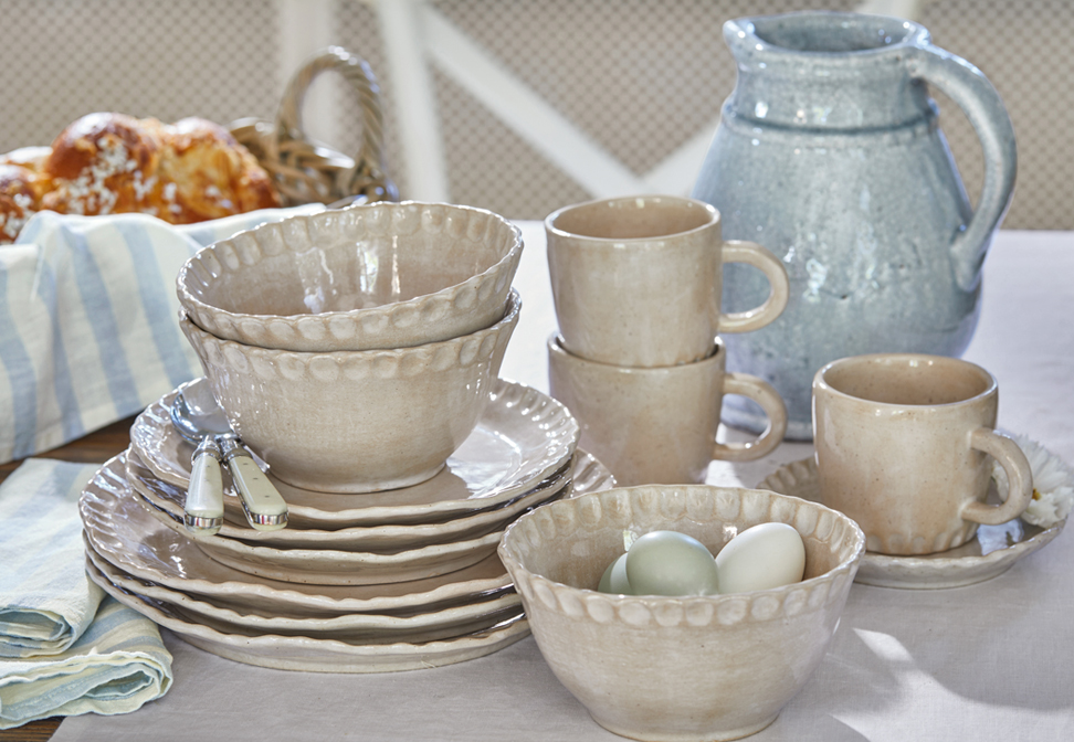 Set di stoviglie in ceramica beige con piatti, ciotole e tazze su tavolo rustico