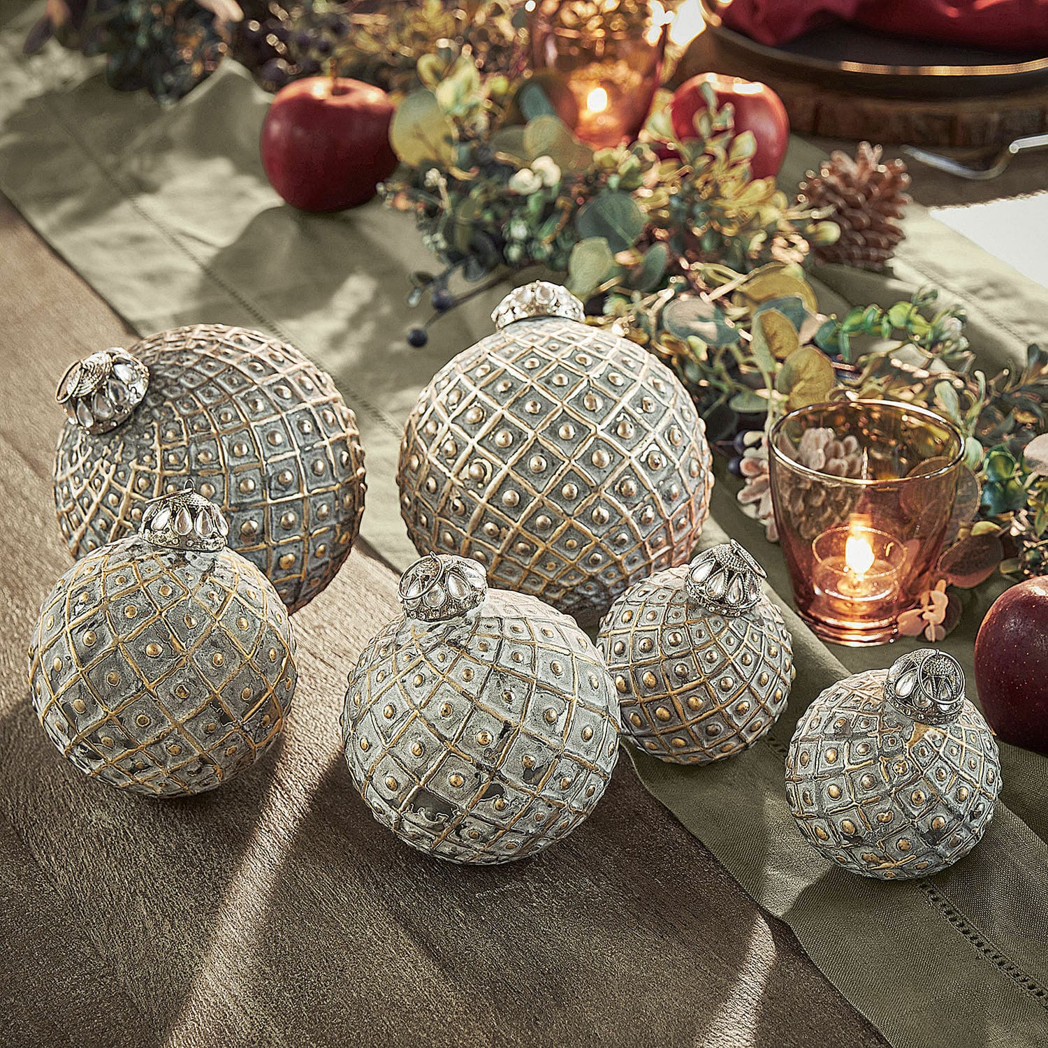 Set di 6 decorazioni natalizie Lucero Set di sei sfere decorative in metallo grigio dorato su tavola festiva con mele e candela accesa