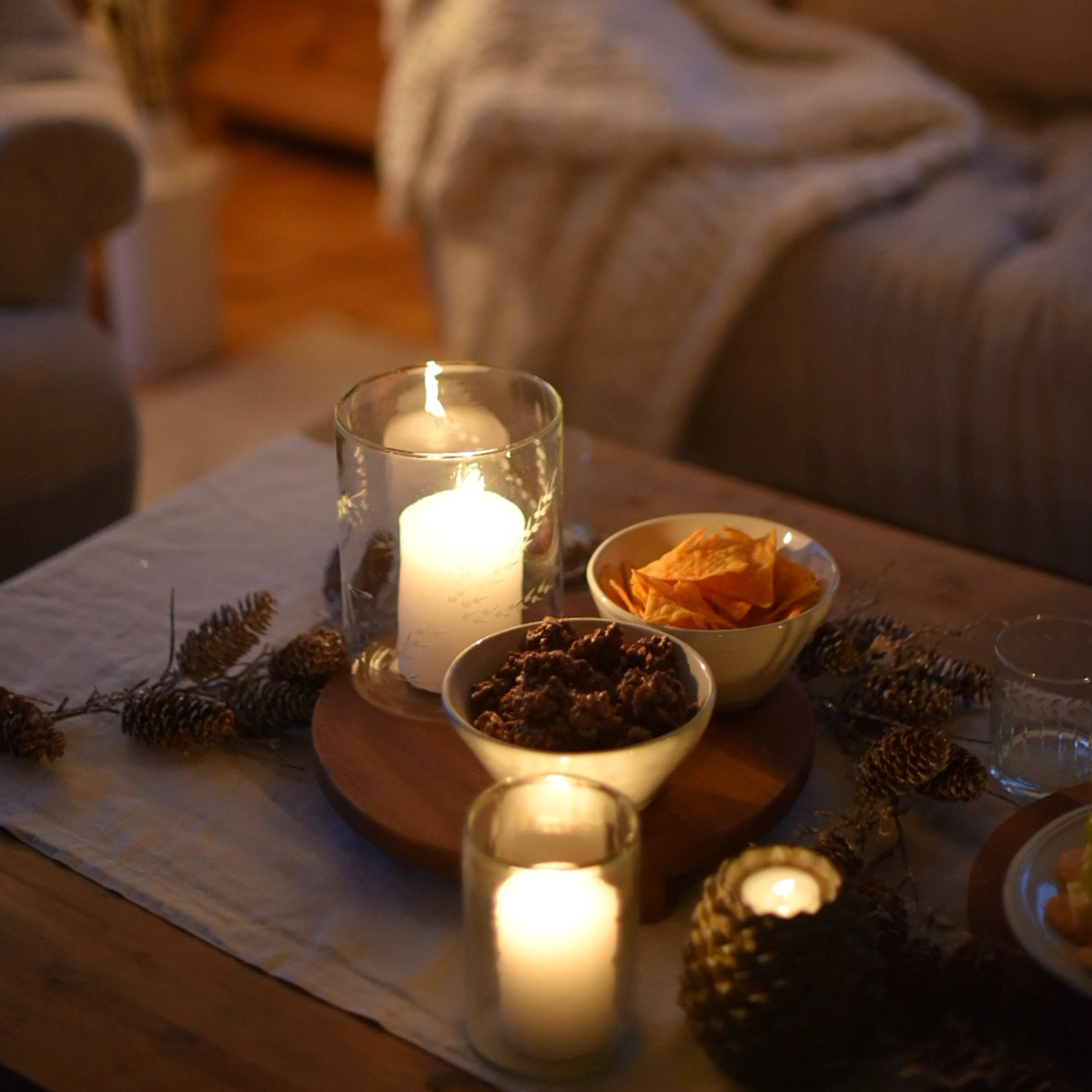 Candele in portacandele di vetro e ciotole con snack su tavolo in legno in ambiente accogliente