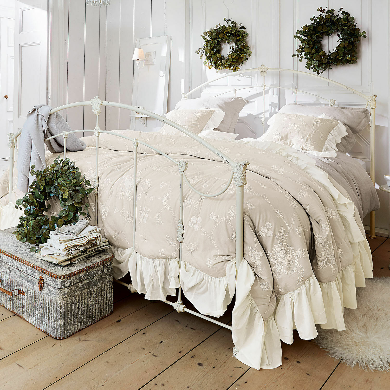 Trapunta Clarissa Biancheria da letto beige ricamata con volant su letto in metallo bianco in camera luminosa con corone verdi