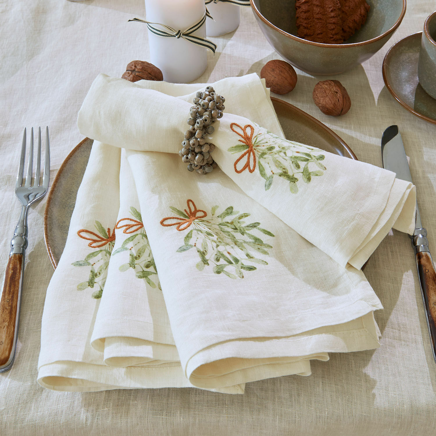 Set di 4 tovaglioli Mistletoe Tovaglioli in lino crema con motivo verde e anello su tavola con stoviglie e noci