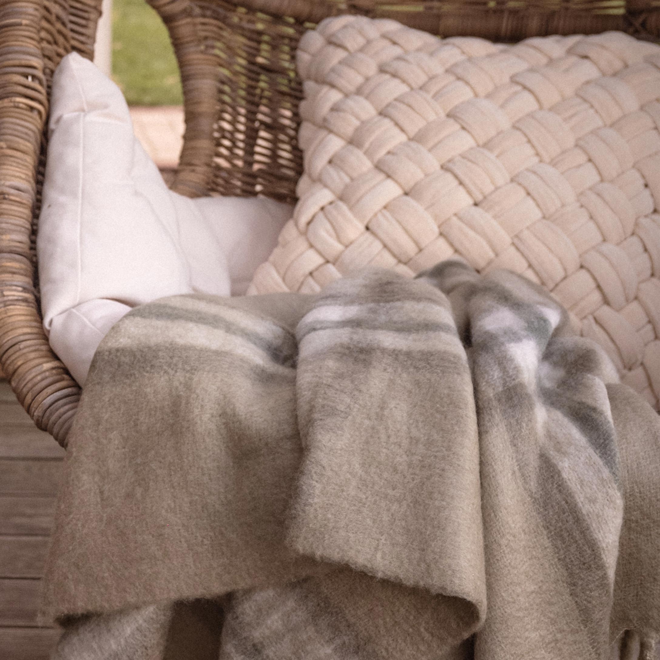 Coperta beige morbida con motivo delicato su poltrona in vimini con cuscini chiari in terrazza