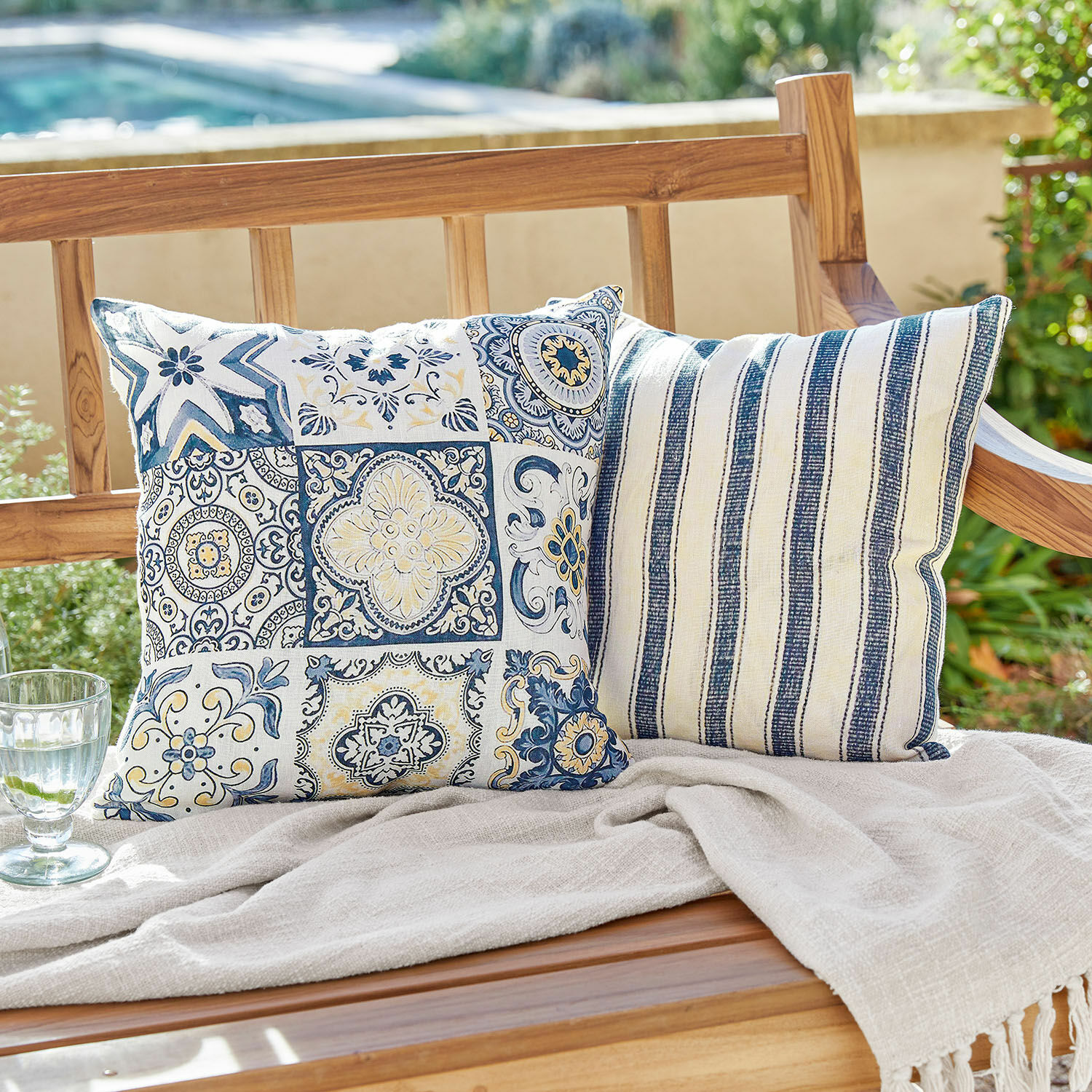 Coppia di copricuscini Bourrignon Due cuscini decorativi in cotone con motivi blu e bianchi su una panca di legno in giardino