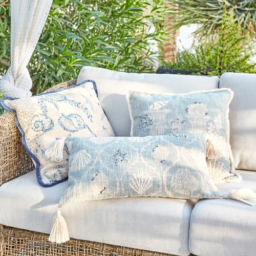 Cuscini decorativi con motivi marini su divano chiaro in rattan in giardino