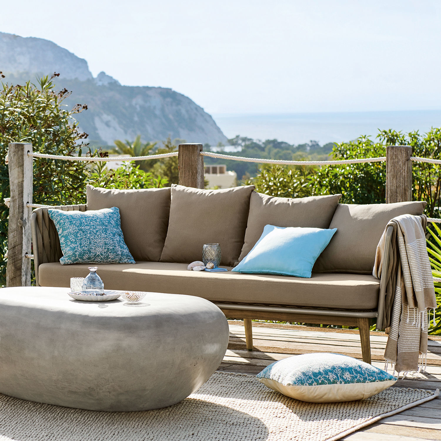 Divano Siochana Divano da esterno beige con cuscini blu e tavolino in pietra grigia su terrazza soleggiata