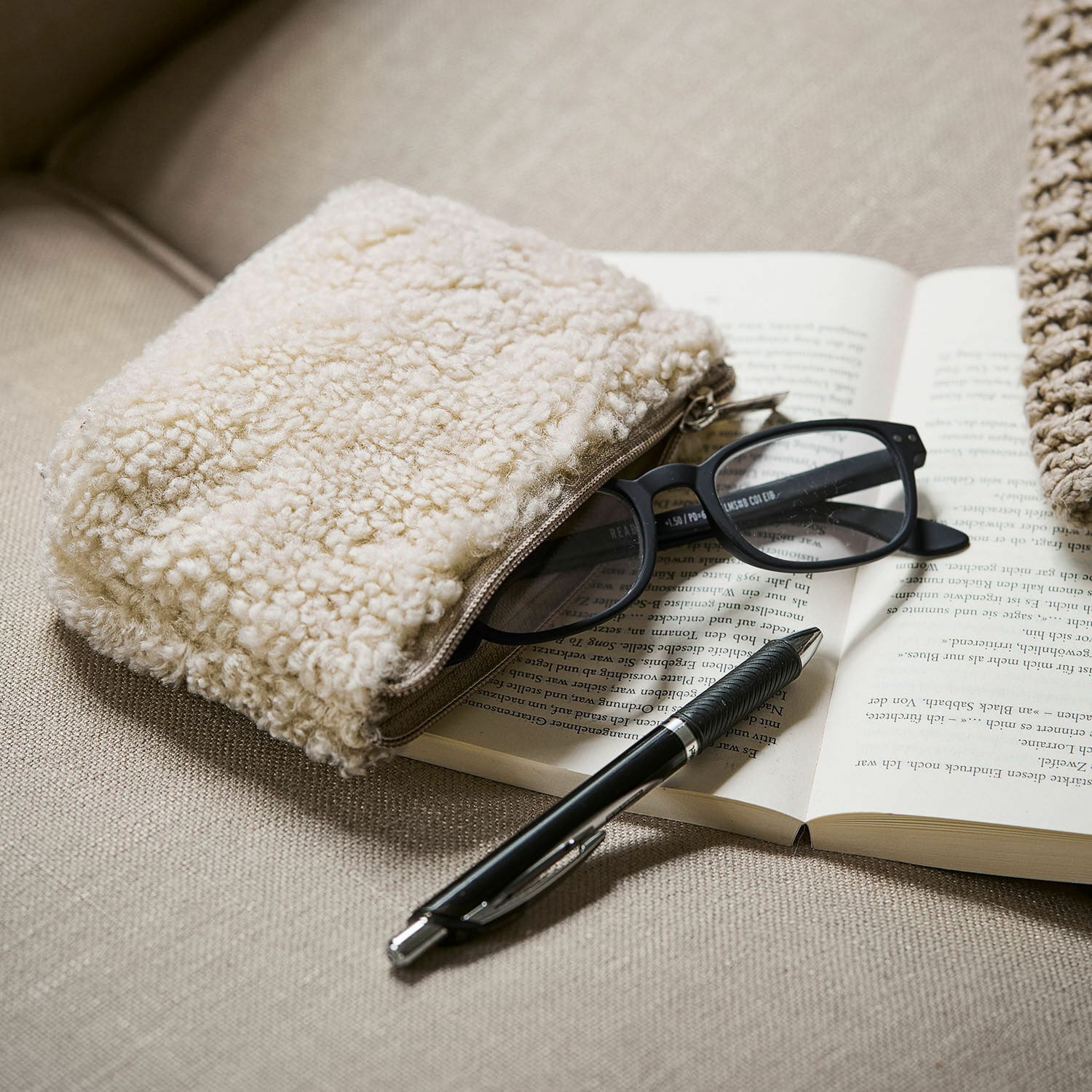 Nécessaire Bathilde Astuccio beige in tessuto effetto orsetto su divano con occhiali e penna nera