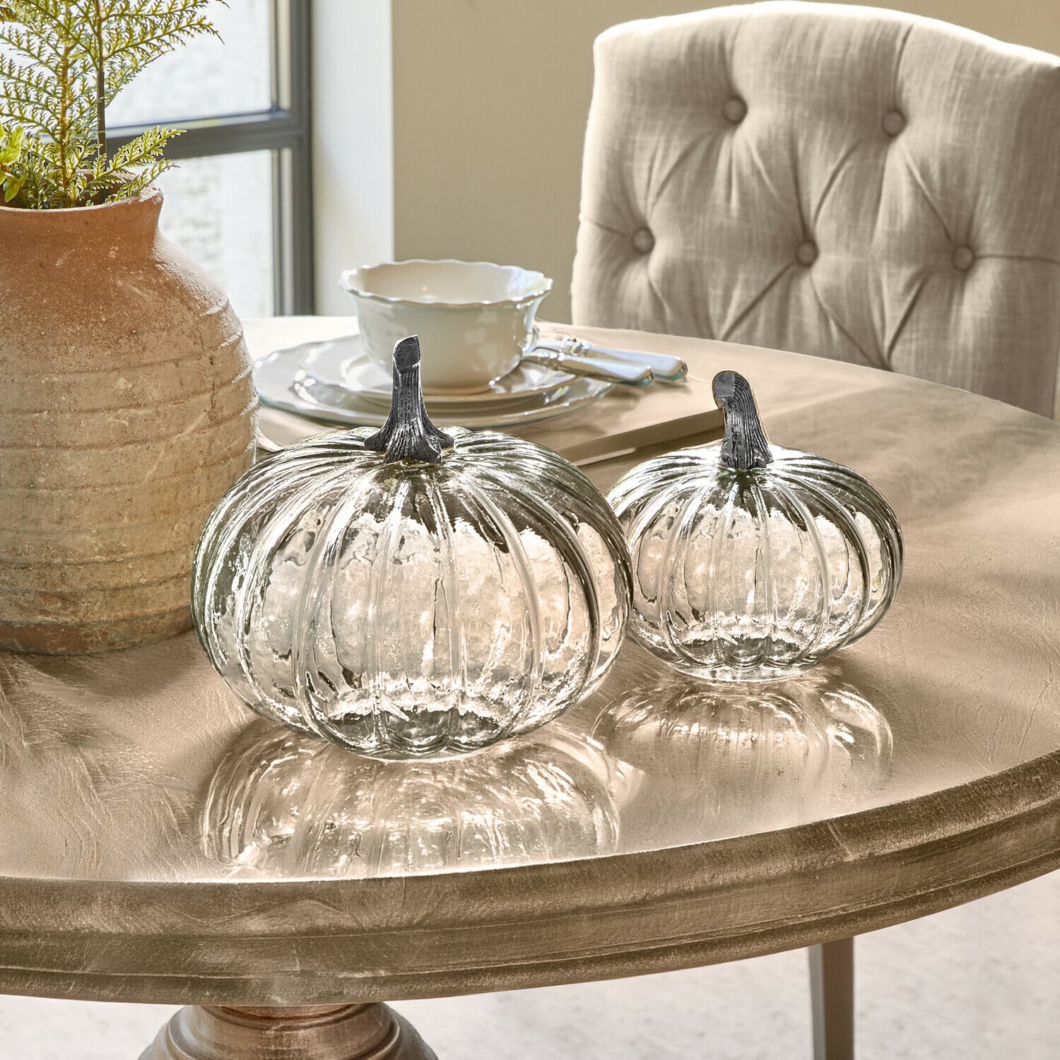 Coppia di zucche Perlouin Due zucche di vetro trasparente con steli metallici su un tavolo decorativo beige