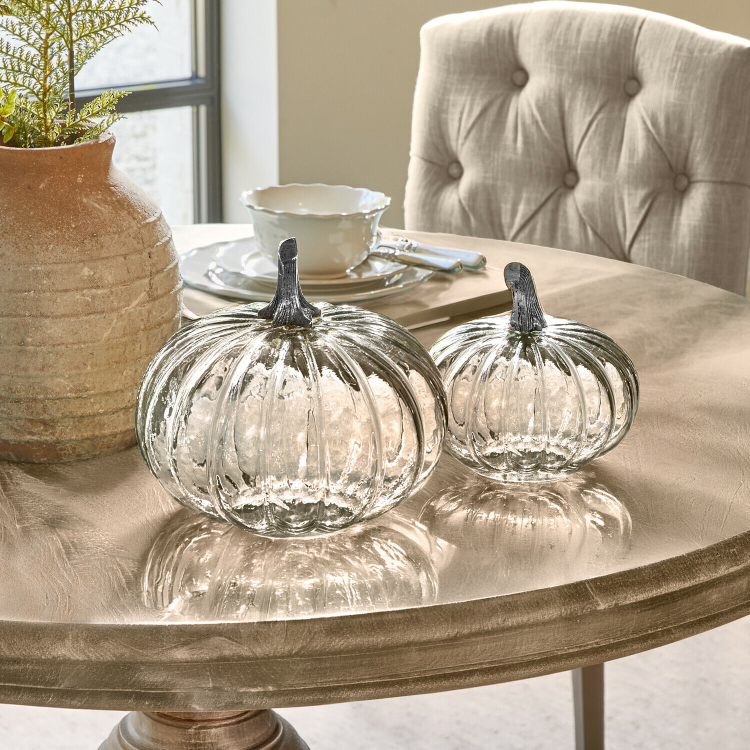 Coppia di zucche Perlouin Due zucche di vetro trasparente con steli metallici su un tavolo decorativo beige
