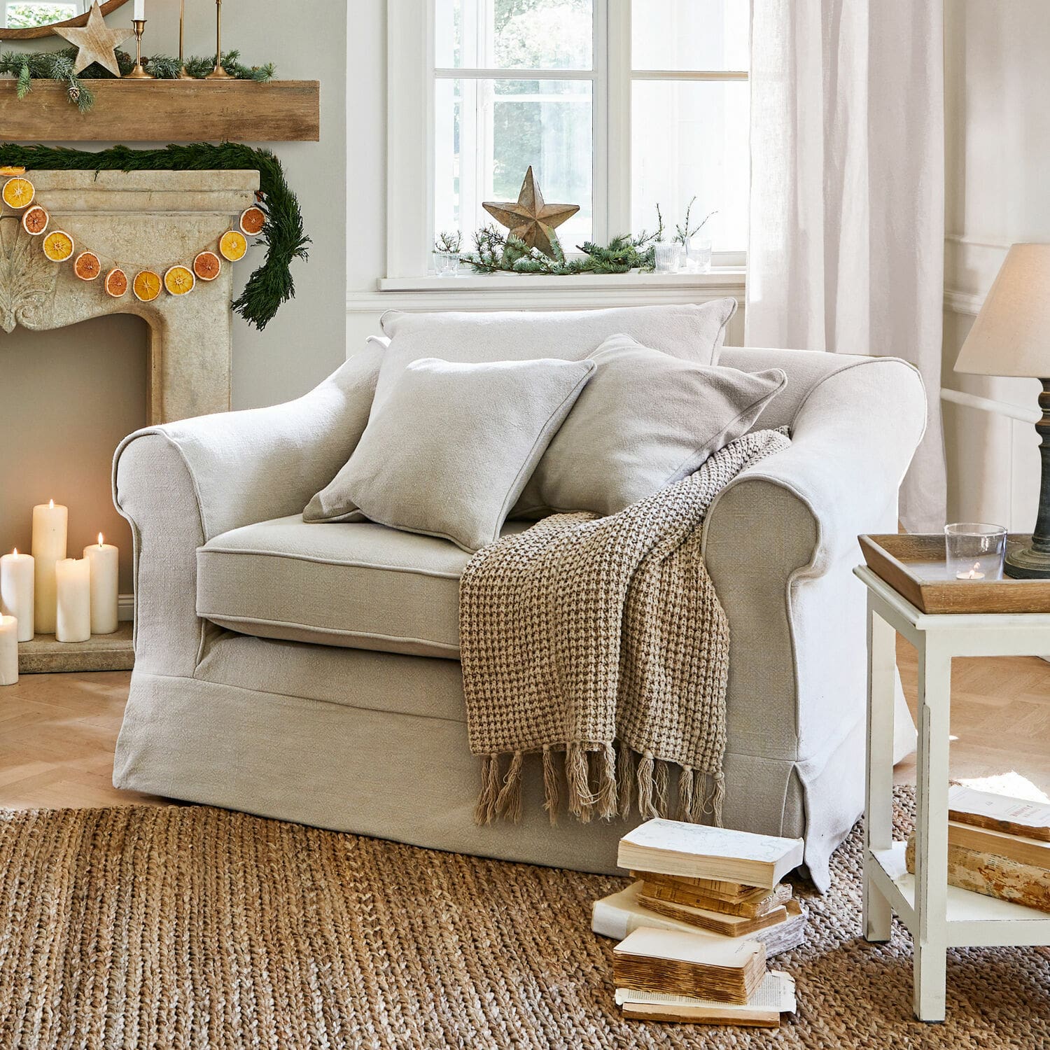 Poltrona Folsom Divano beige in tessuto con cuscini e coperta lavorata su tappeto in juta in soggiorno accogliente