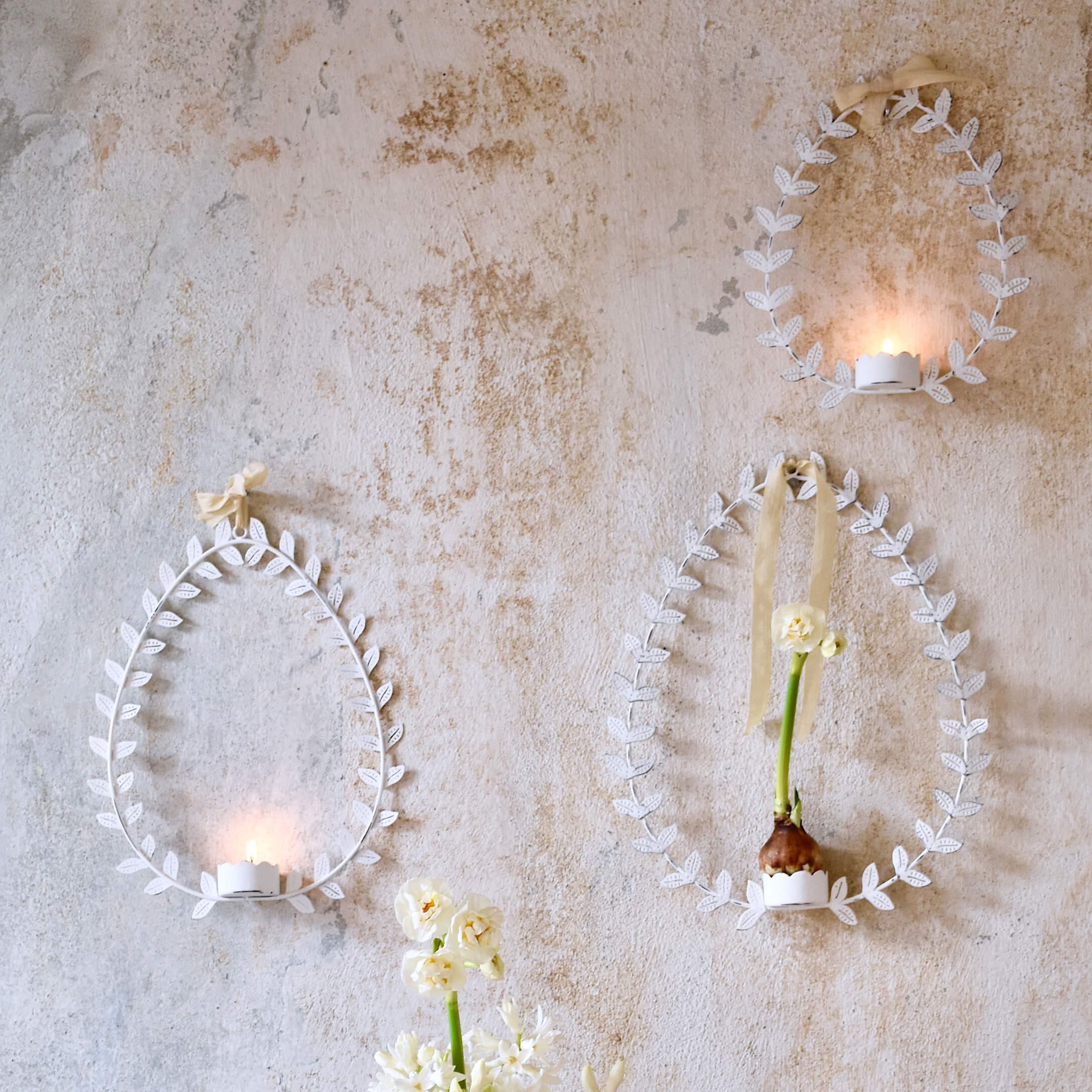 Decorazioni da parete bianche in metallo a forma di uovo con foglie, portacandele e fiori su muro pastello