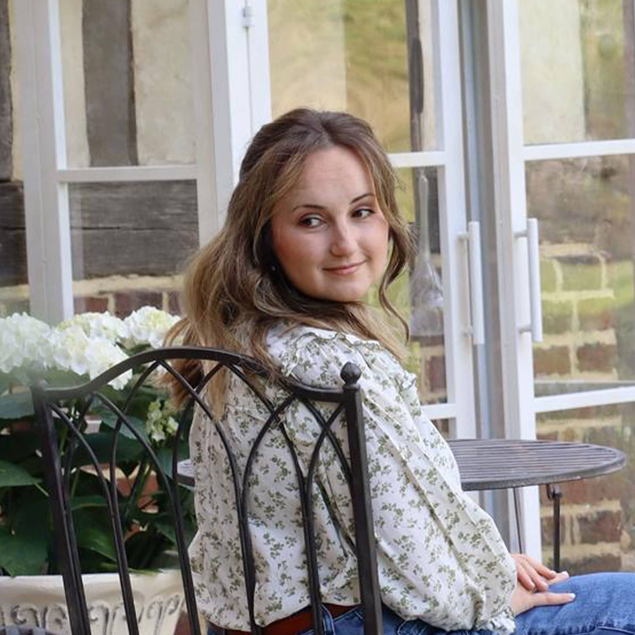 Donna con camicetta floreale seduta su sedia in metallo in giardino luminoso con fiori bianchi