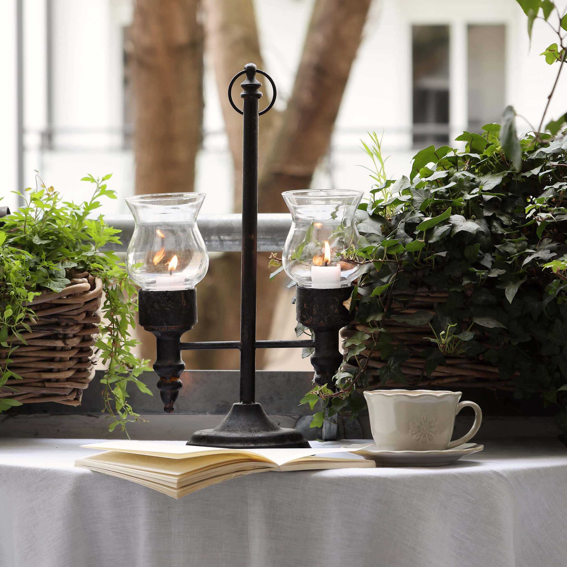 Portacandele in metallo con due coperture in vetro tra piante verdi su balcone