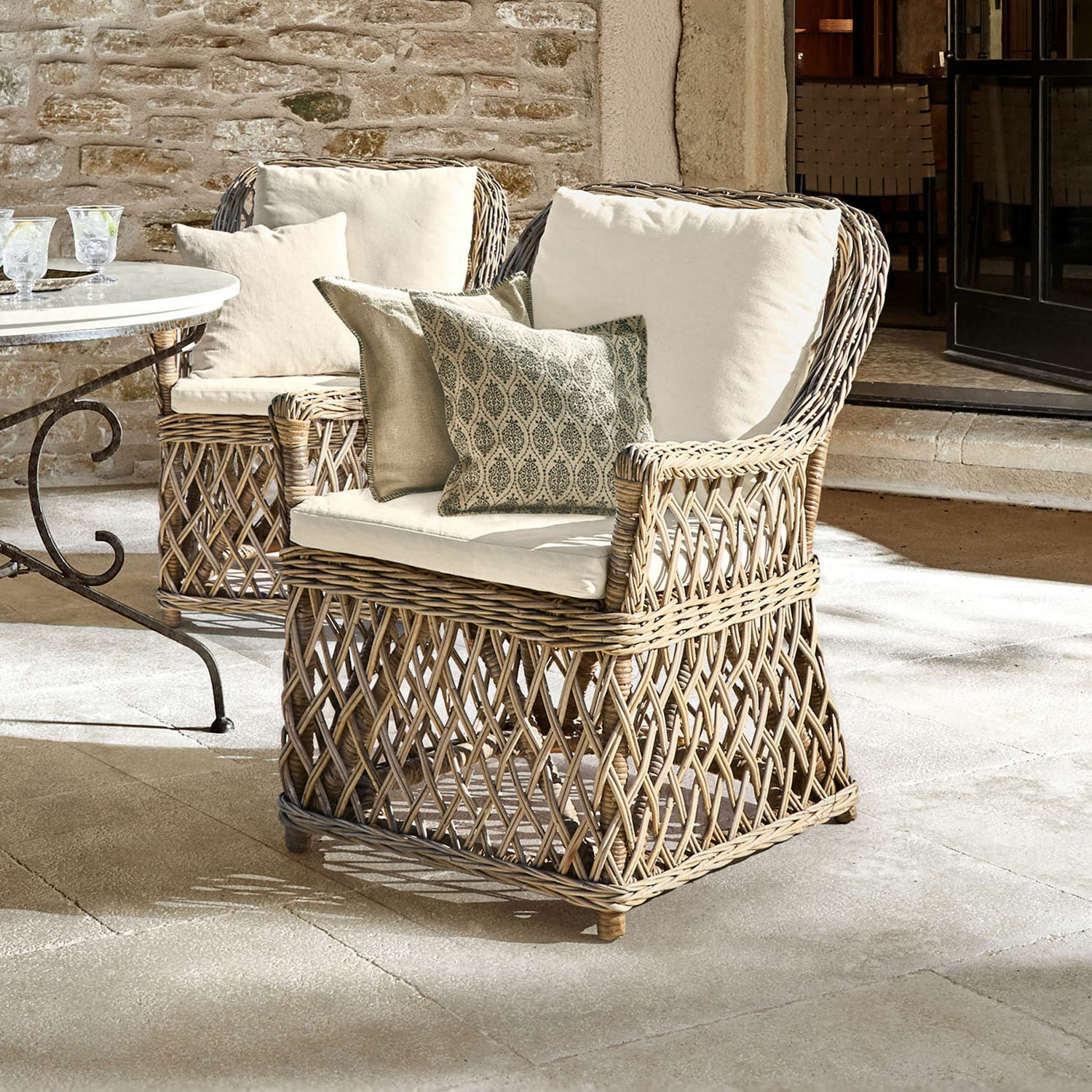 Poltrona Nesvryn Poltrona confortevole in rattan naturale con cuscini crema e cuscini decorativi per esterni eleganti.