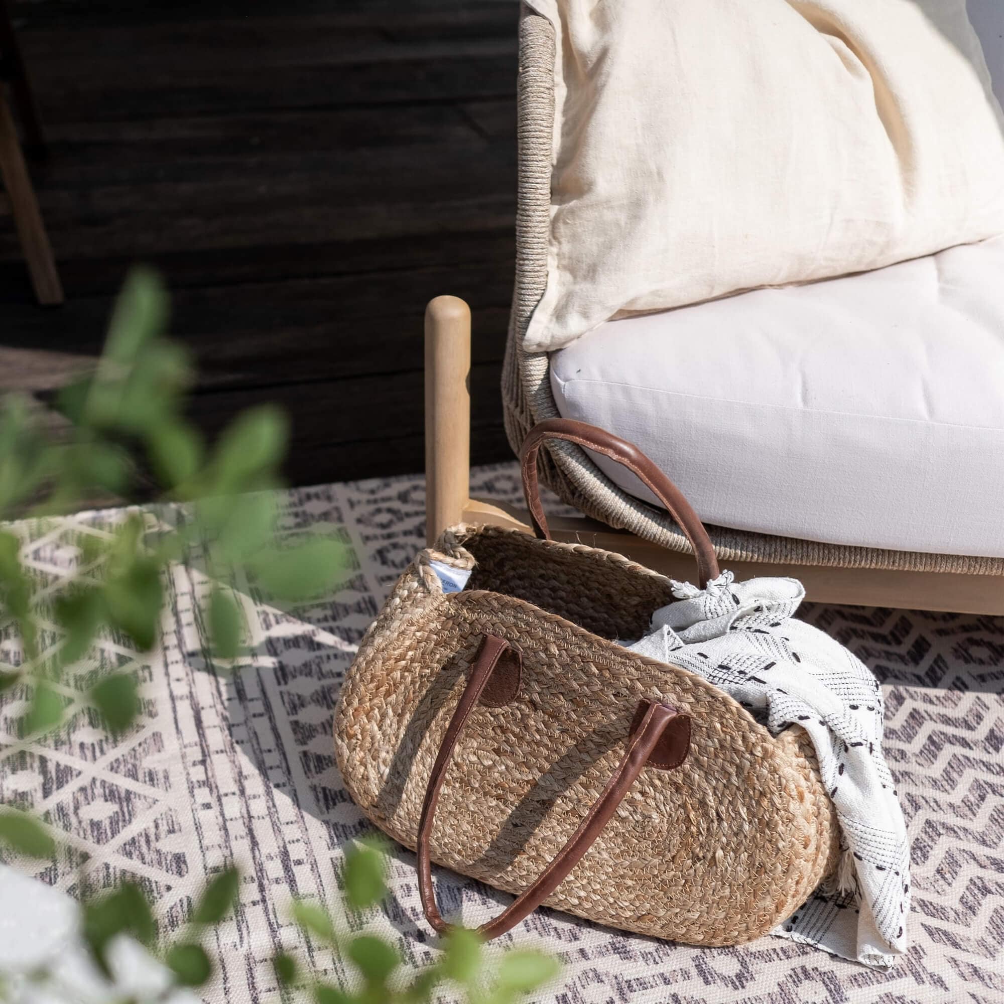 Borsa ovale in paglia intrecciata con manici marroni e tessuto bianco su tappeto decorato