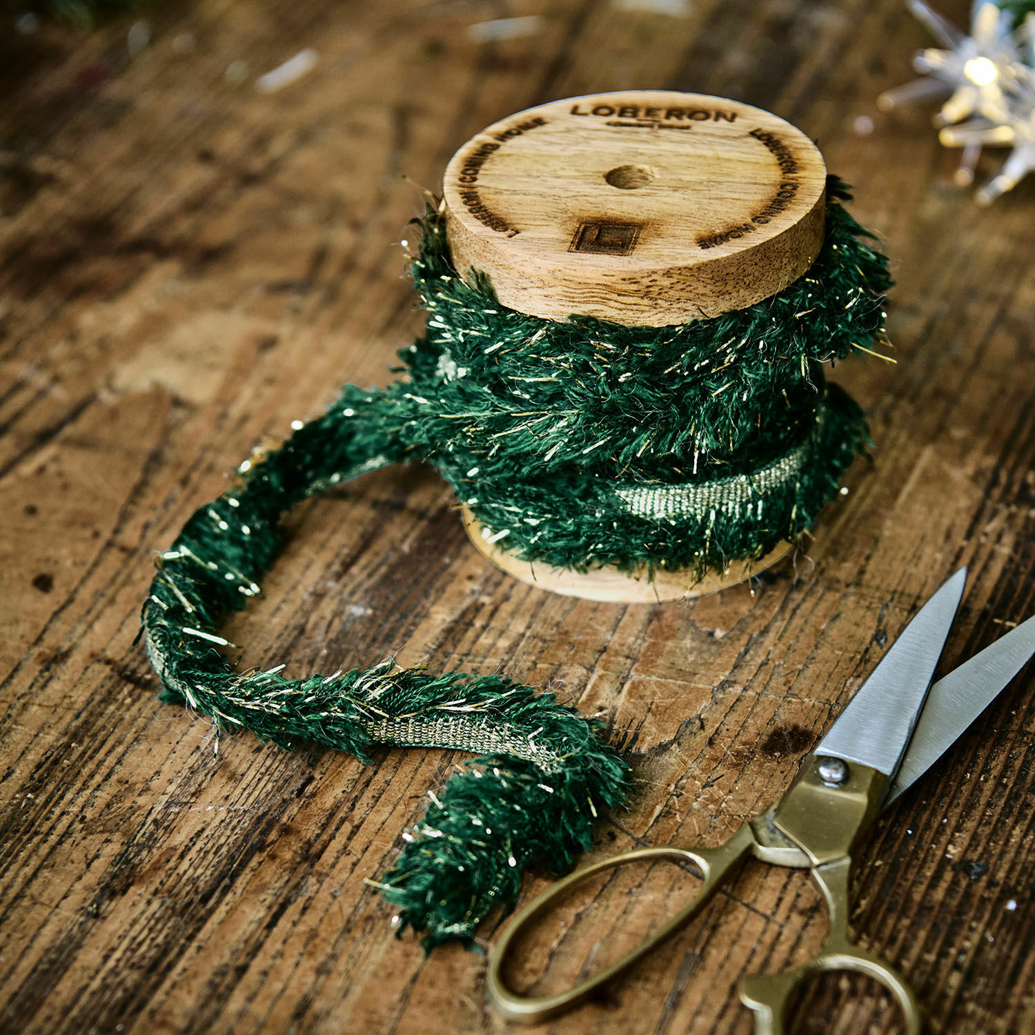 Nastro Calarith Nastro decorativo verde con fili metallici su rocchetto di legno accanto a forbici su tavolo in legno