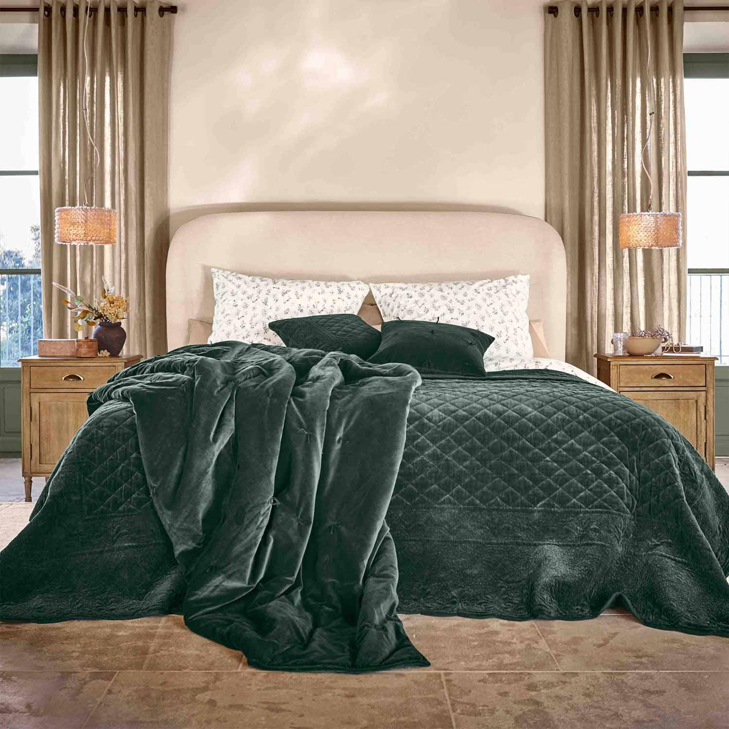 Coperta e cuscini in velluto verde scuro su letto con testiera beige in camera accogliente