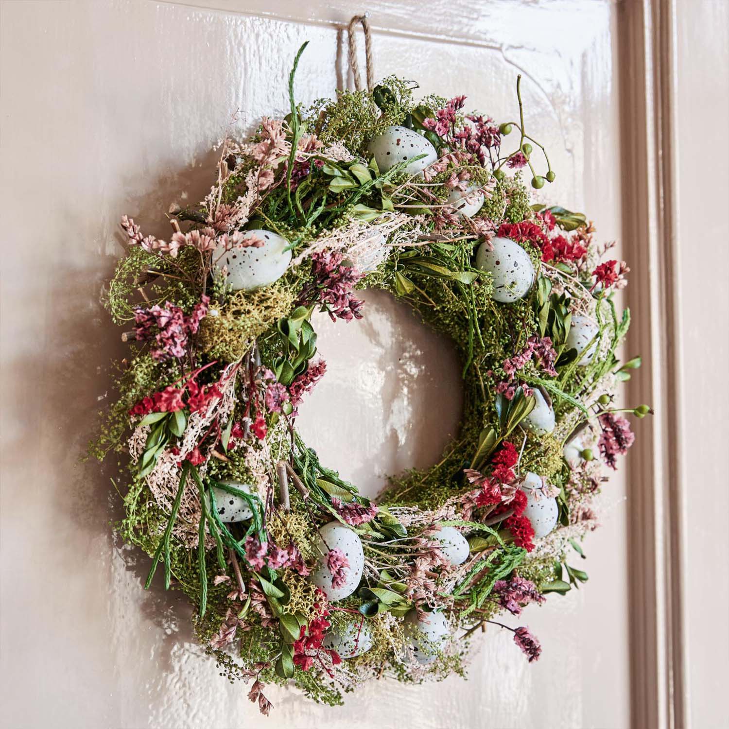 Corona decorativa con rami verdi, fiori rosa e uova finte azzurre appesa alla porta