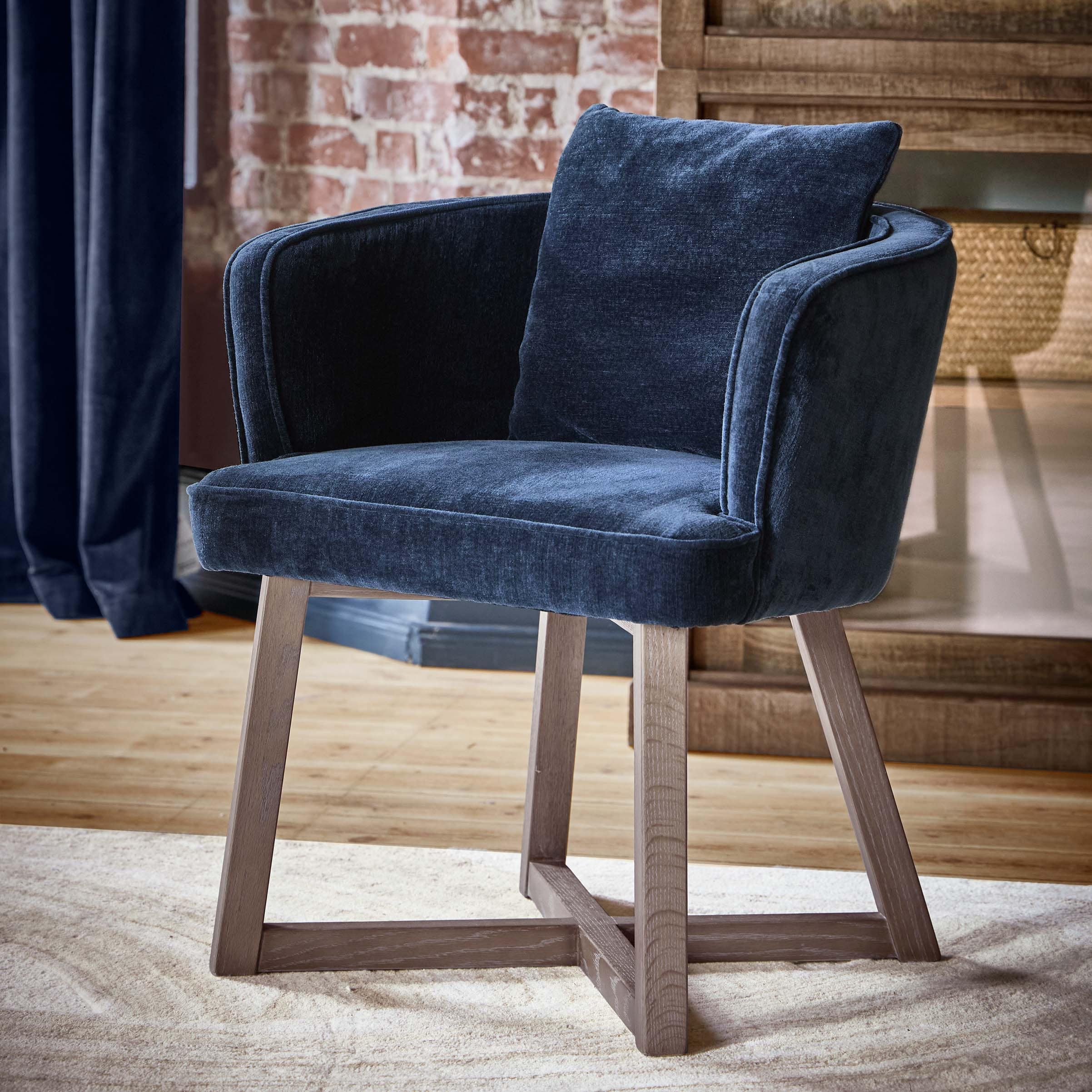 Poltrona blu scuro in tessuto morbido con gambe in legno in interno elegante con muro in mattoni