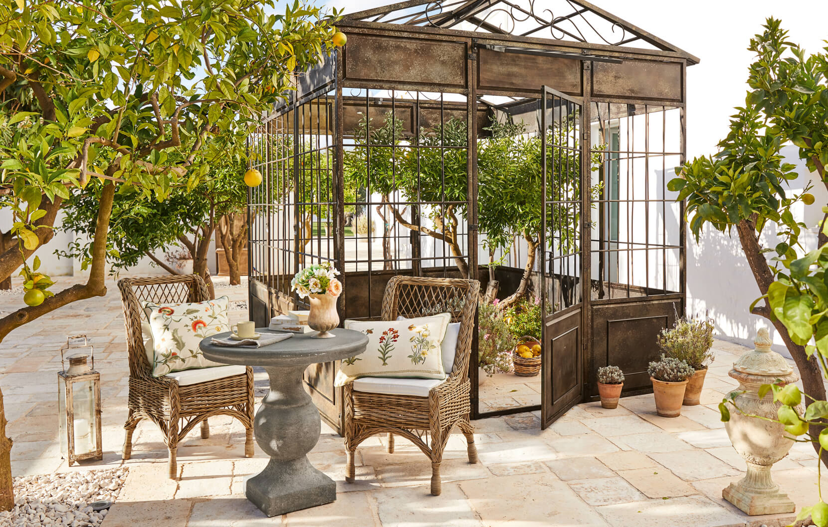 Giardino mediterraneo con gazebo in metallo, sedie in vimini e tavolo in pietra sulla terrazza