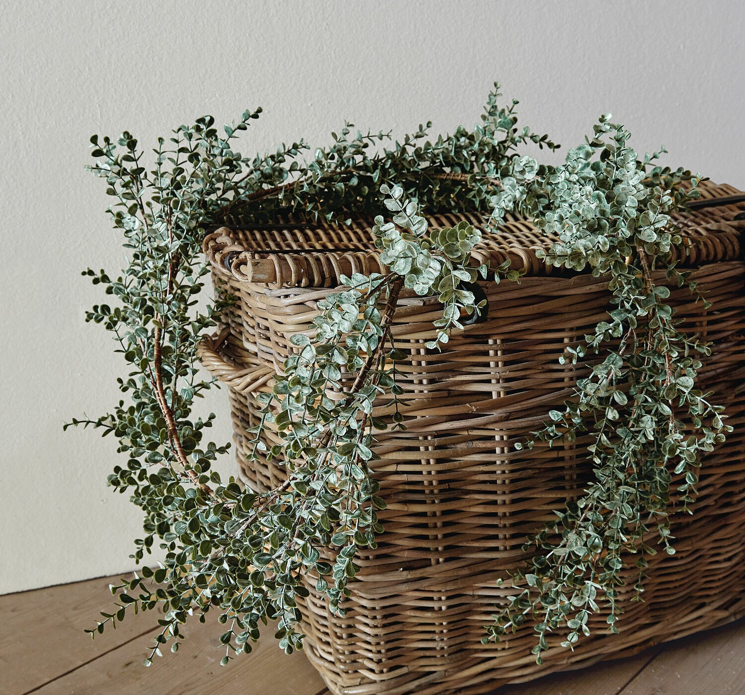 Corona decorativa di foglie verdi di eucalipto su cesta di vimini su pavimento in legno