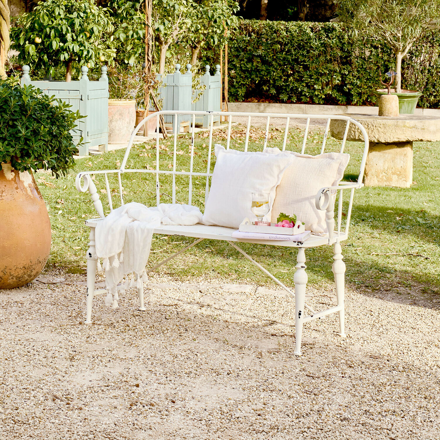 Panchina da giardino in metallo bianco con cuscini e coperta su patio ghiaioso in giardino verde