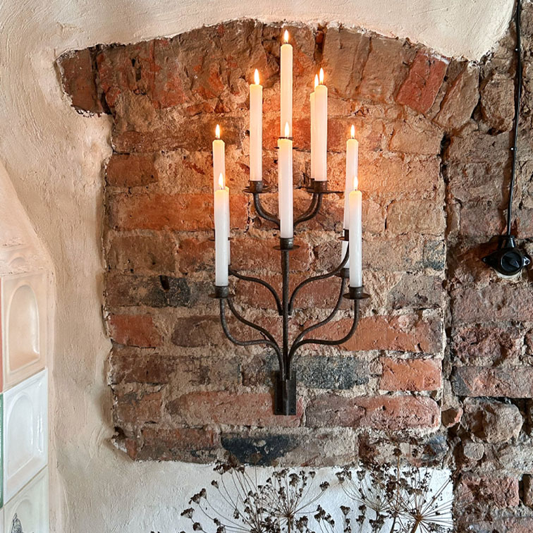 Portacandele da parete in metallo con sette candele bianche accese su muro di mattoni, decorazione