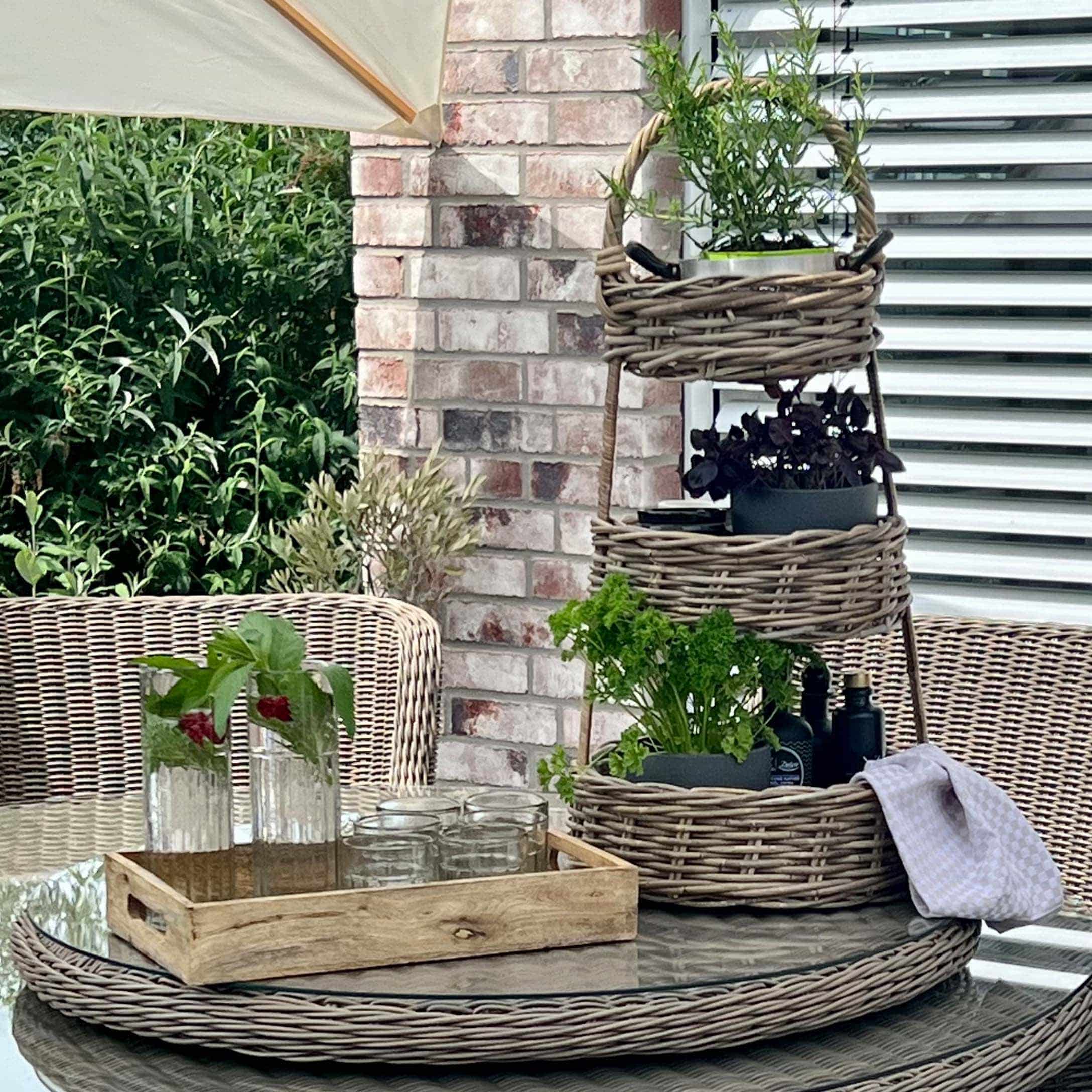 Porta piante a tre livelli in vimini con piante verdi su tavolo in vetro su terrazza con mobili in rattan