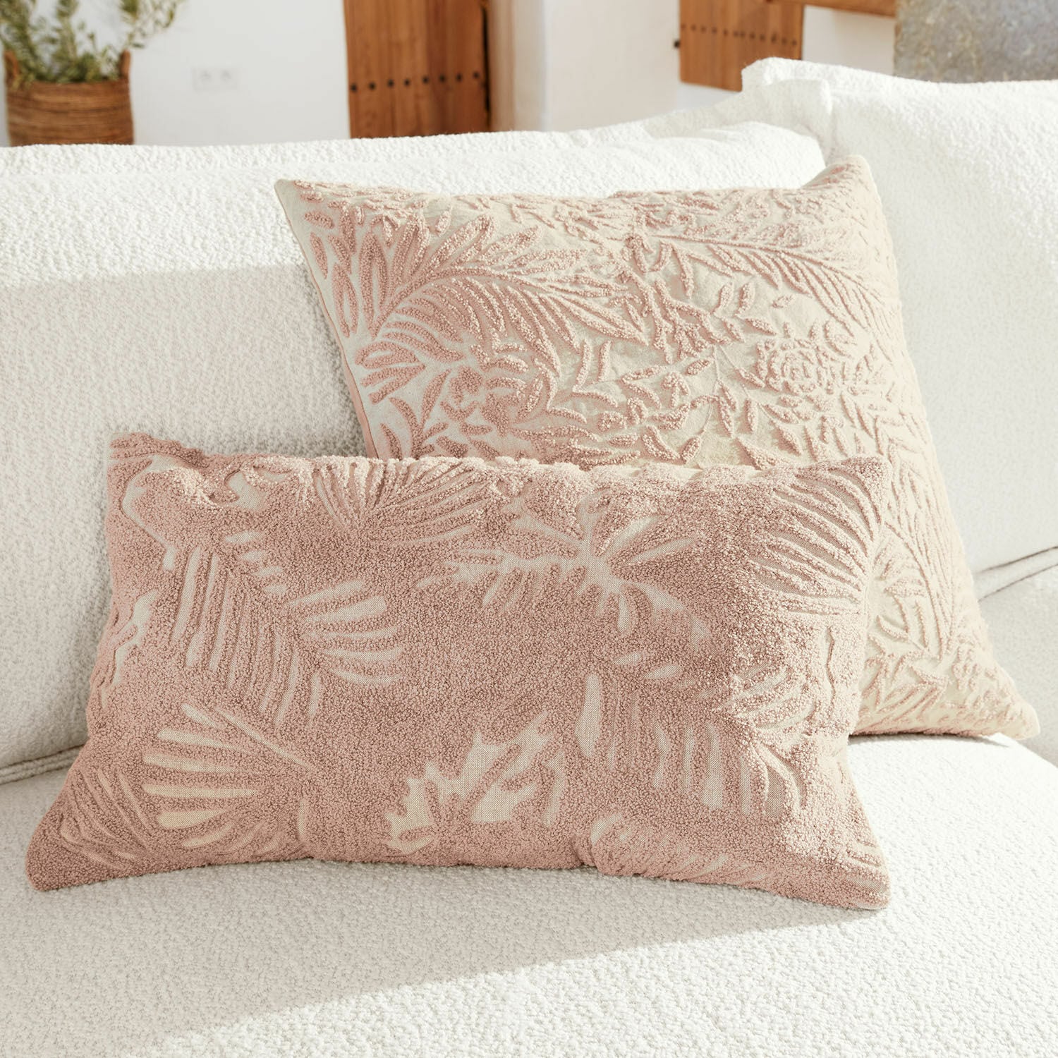 Coppia di copricuscini Enchanto Due cuscini decorativi con motivo foglie rosa su sfondo crema su divano bianco
