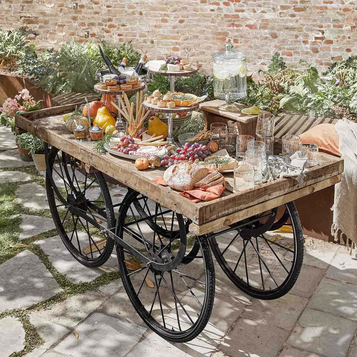 Carretto rustico in legno con ruote nere carico di snack e bevande in giardino soleggiato