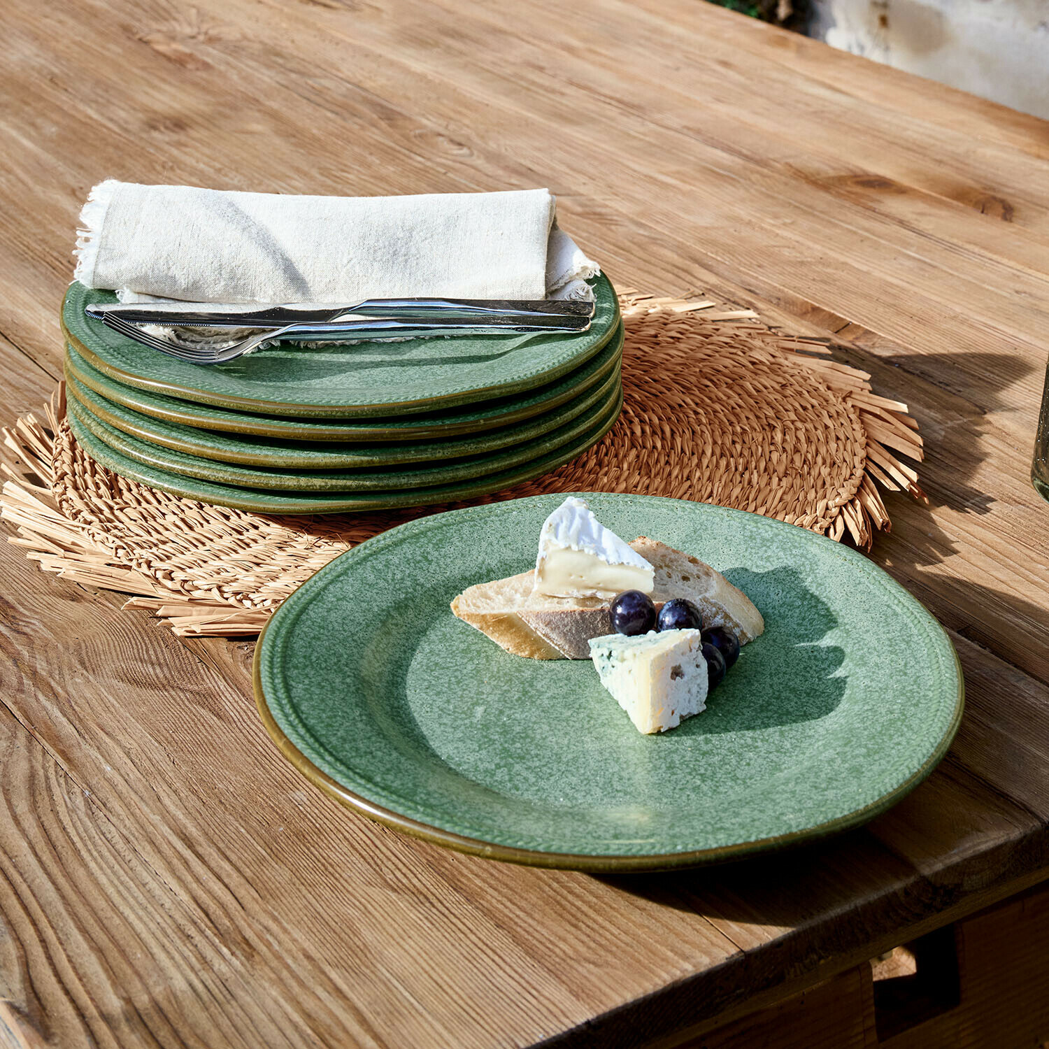 Set di piatti in ceramica verde su tavolo in legno con formaggio, uva e pane