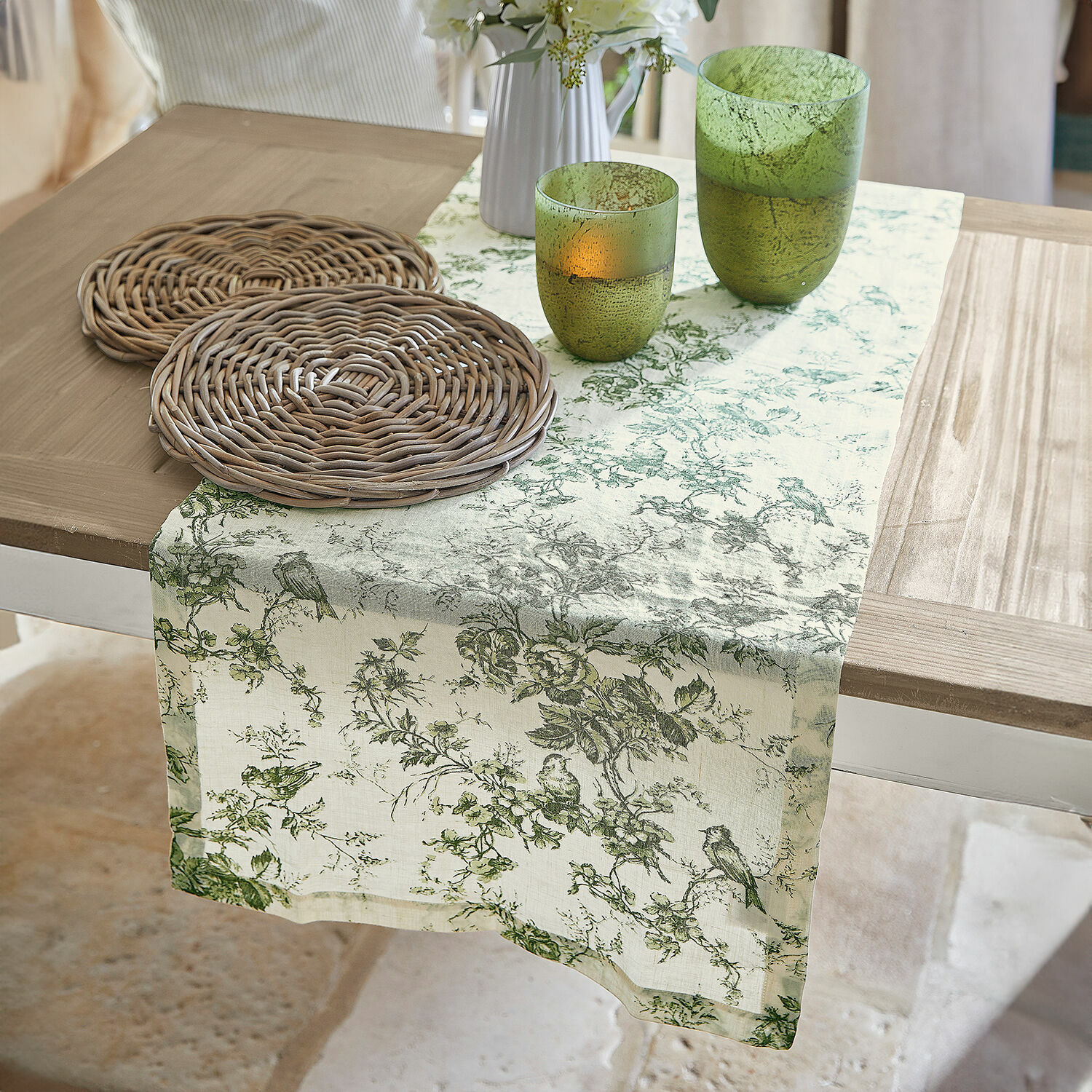 Runner Mercier Runner da tavola in lino con motivo vegetale verde su tavolo in legno con sottobicchieri in vimini e bicchieri verdi