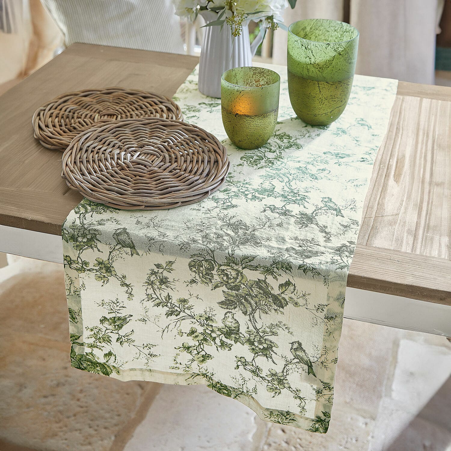 Runner Mercier Runner da tavola in lino con motivo vegetale verde su tavolo in legno con sottobicchieri in vimini e bicchieri verdi