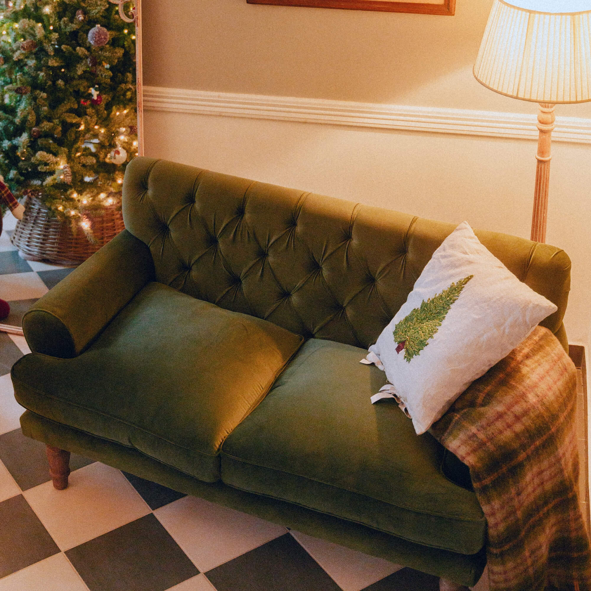 Divano verde in velluto con schienale capitonné, cuscino bianco con albero di Natale e plaid in soggiorno