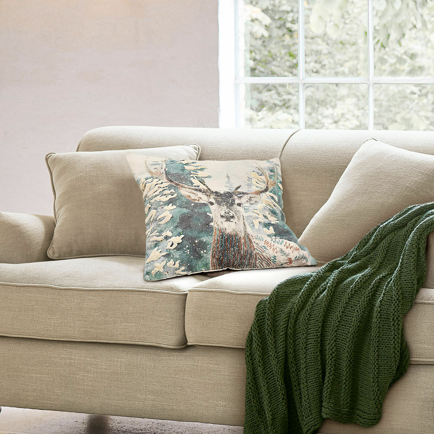 Copricuscino Elvaris Divano beige con cuscino decorativo con cervo e coperta verde lavorata a maglia in soggiorno