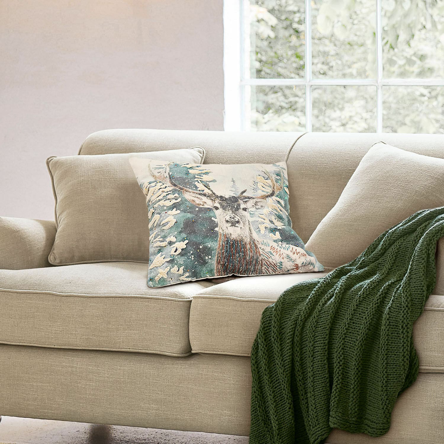 Copricuscino Elvaris Divano beige con cuscino decorativo con cervo e coperta verde lavorata a maglia in soggiorno