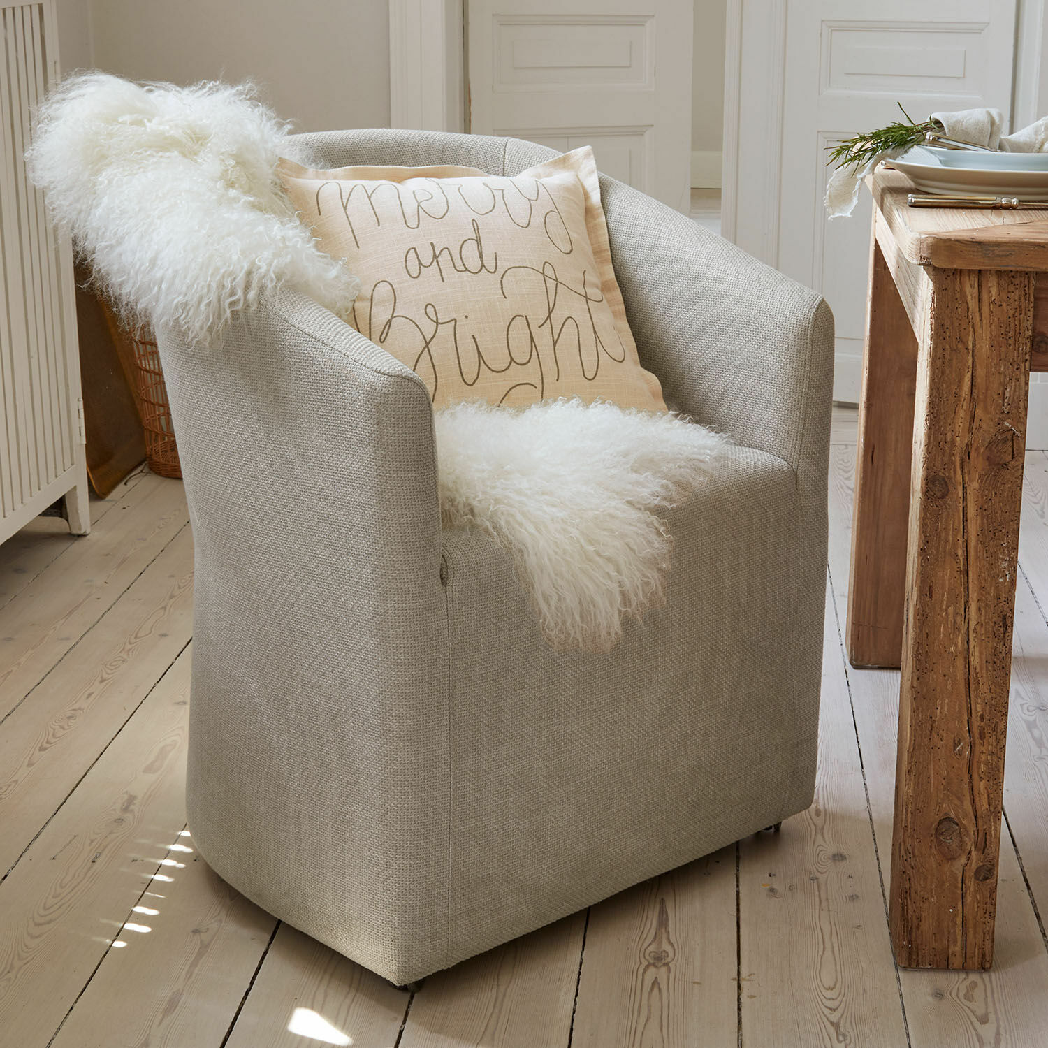 Poltrona Holmsen Poltrona grigia rivestita con morbida coperta bianca e cuscino decorativo chiaro in stile scandinavo