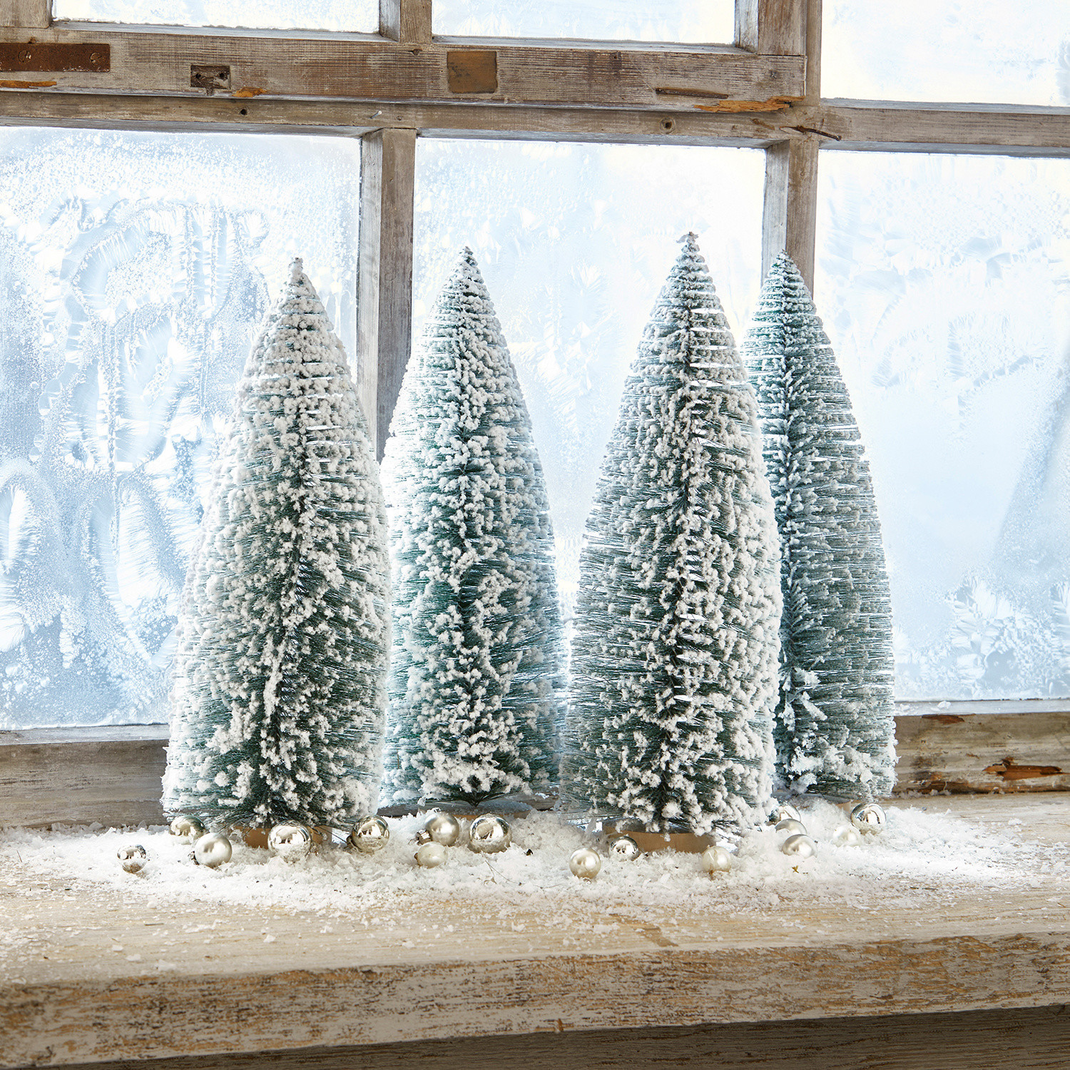 Set di 4 alberelli decorativi Landscape Quattro alberi di plastica verdi a forma conica con neve bianca su un davanzale in legno con palline decorative