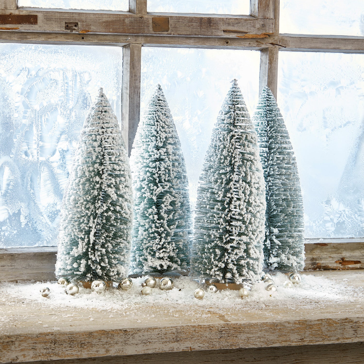 Set di 4 alberelli decorativi Landscape Quattro alberi di plastica verdi a forma conica con neve bianca su un davanzale in legno con palline decorative