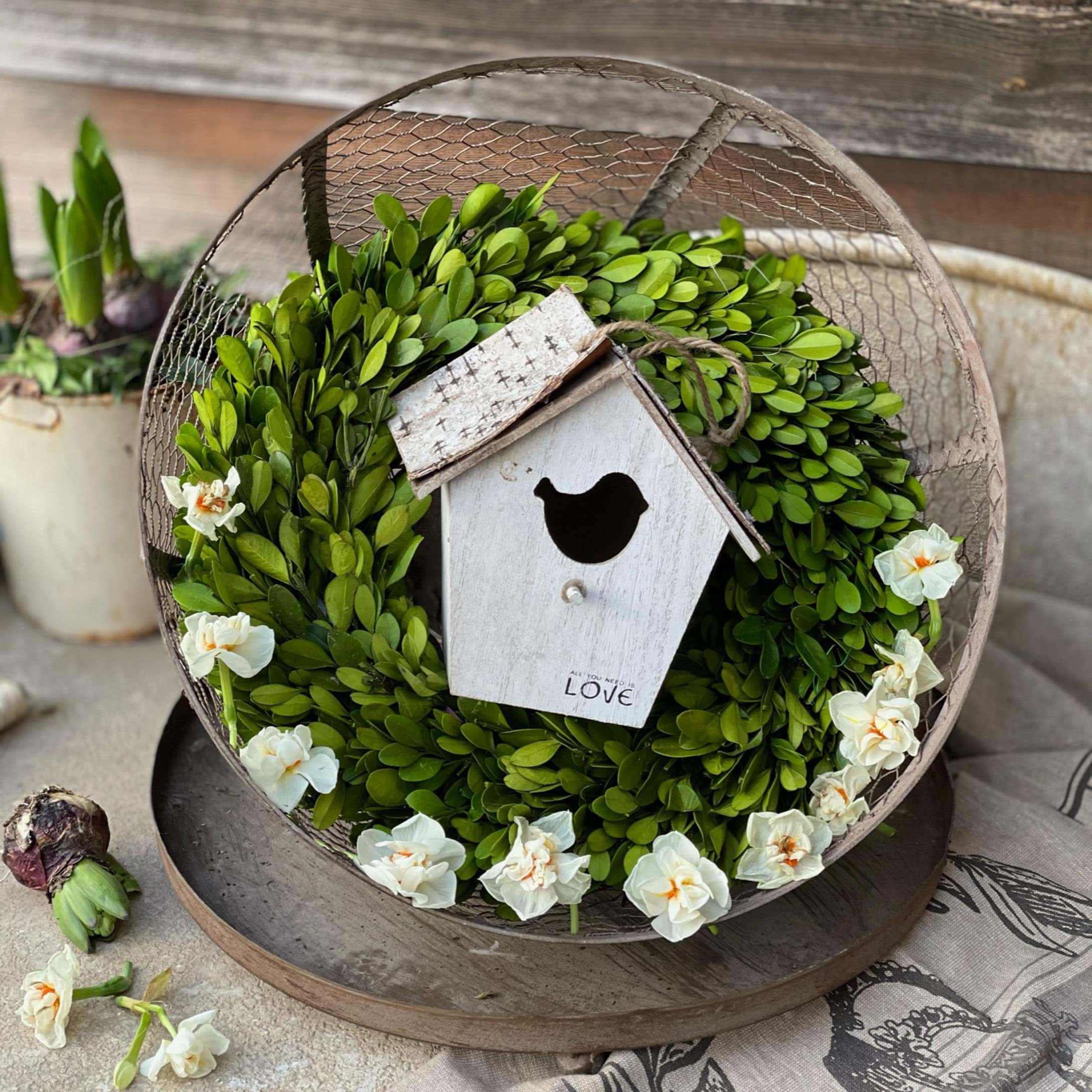 Corona decorativa di foglie verdi e fiori bianchi con casetta per uccelli in legno su tavolo rustico