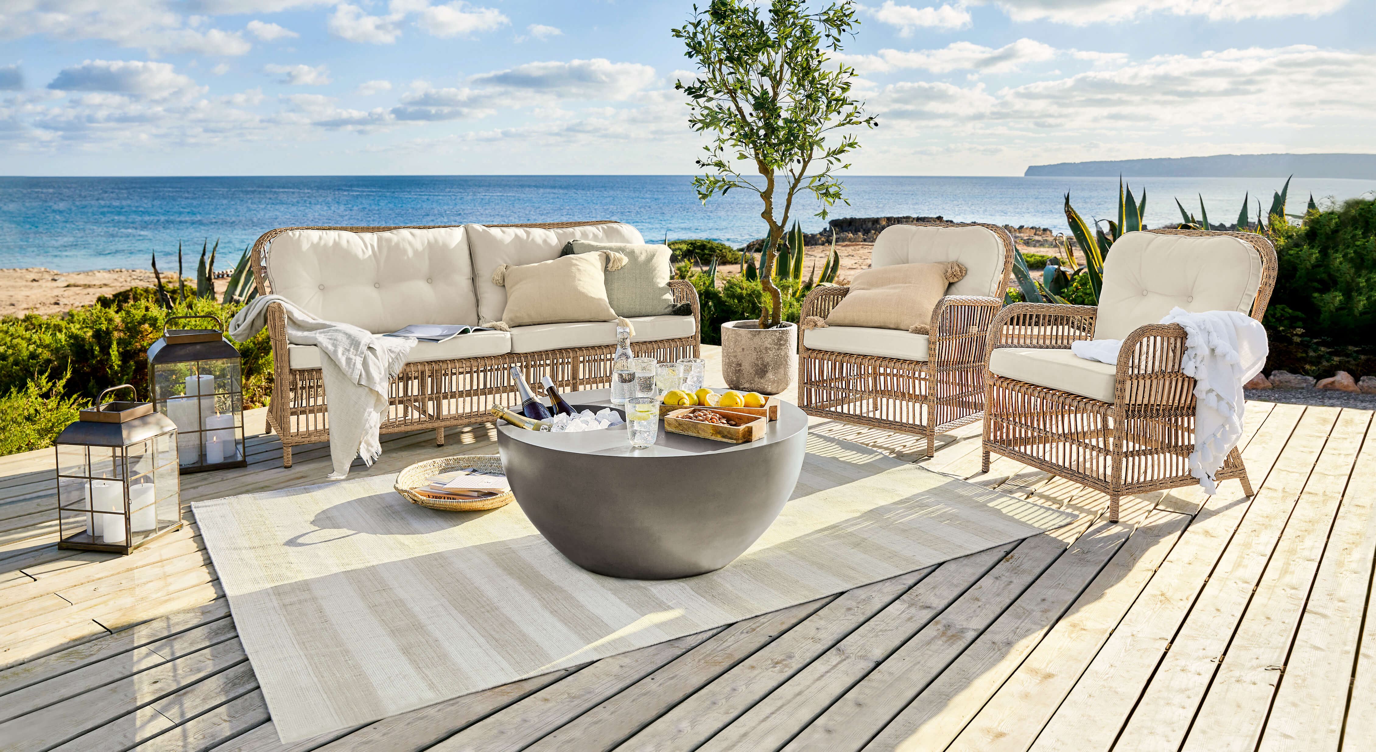 Set di mobili da giardino in rattan con cuscini crema su terrazza in legno vista mare