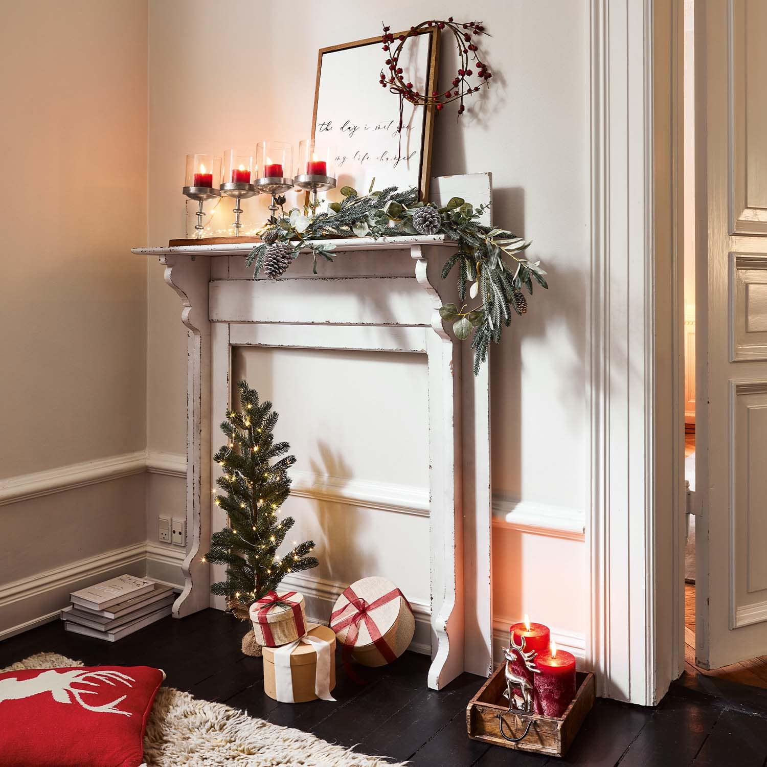 Camino bianco in legno decorato per Natale con candele rosse e regali incartati sul pavimento