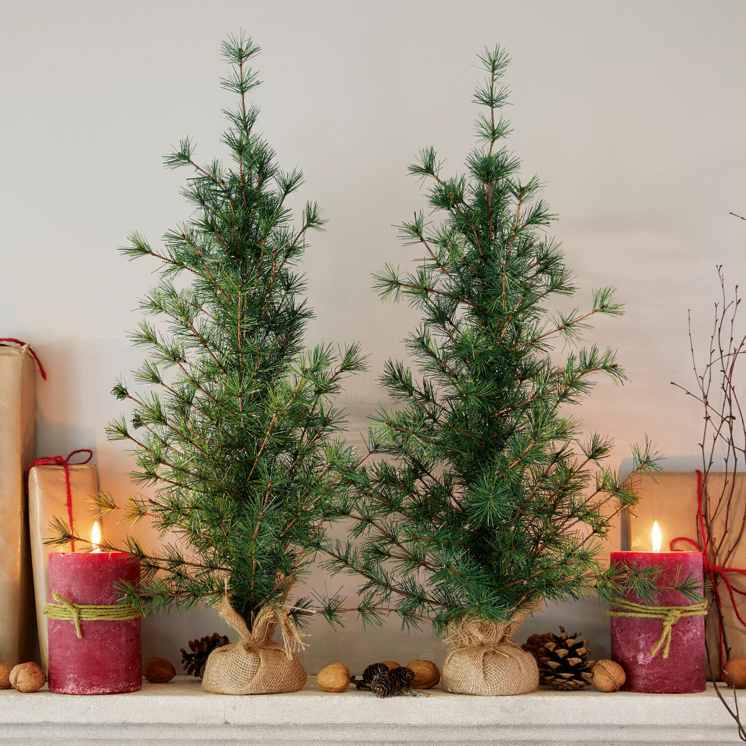 Coppia di alberelli decorativi Bohicon Due piccoli alberi di Natale verdi in sacchi di juta con candele rosse e noci sul camino